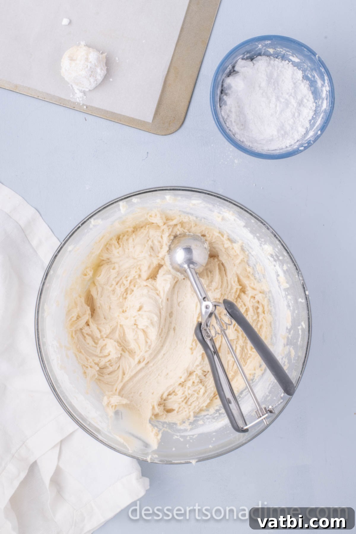 A cookie scoop forming uniform dough balls to be rolled in powdered sugar.