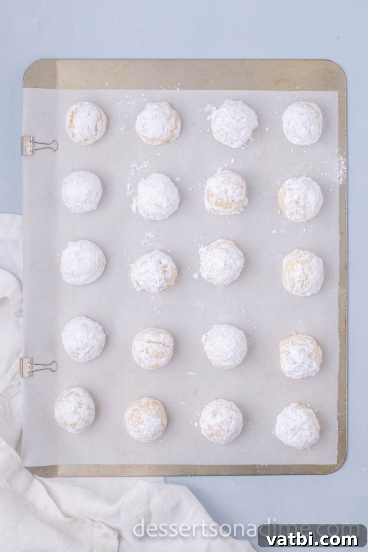 Powdered sugar-coated cookie dough balls neatly arranged on a baking sheet.