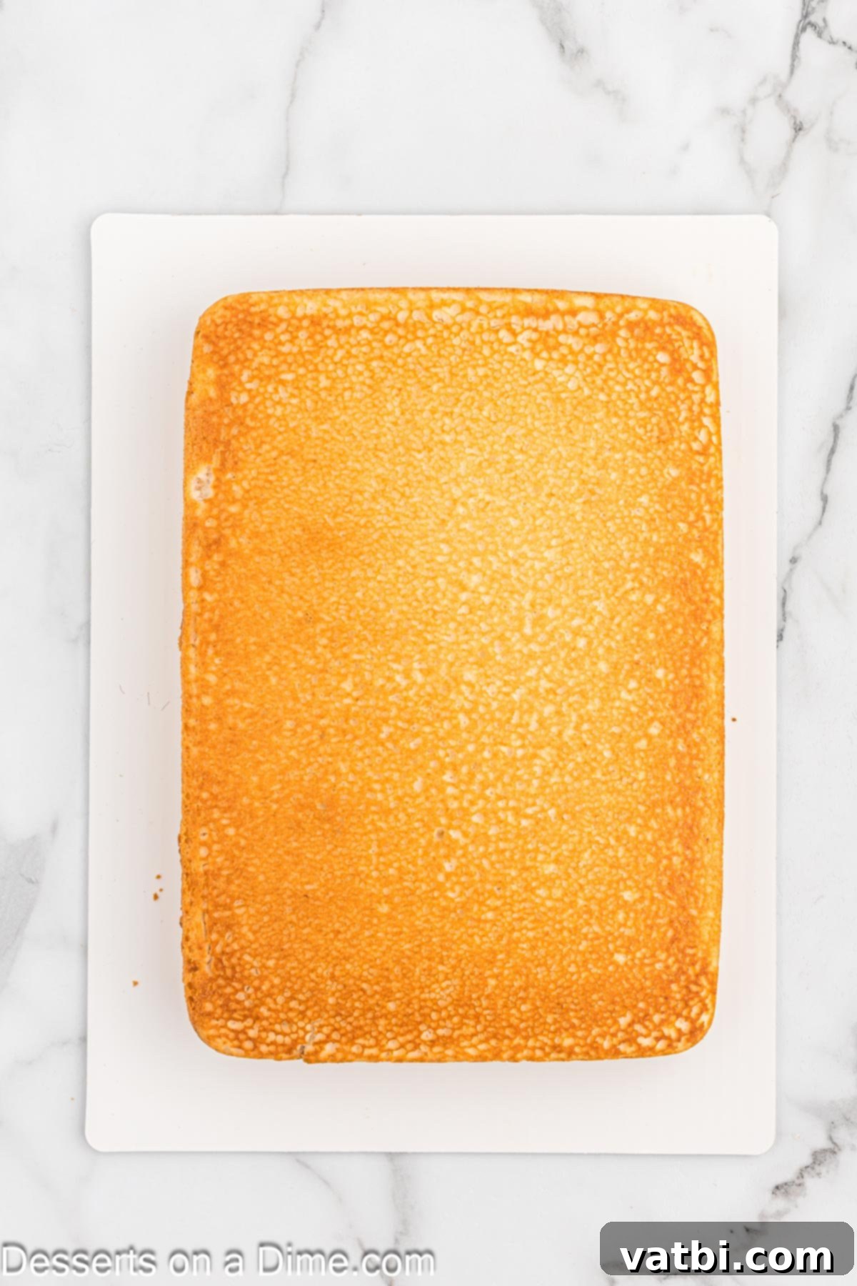 Freshly baked cake cooling on wax paper on a kitchen counter after being removed from the pan.