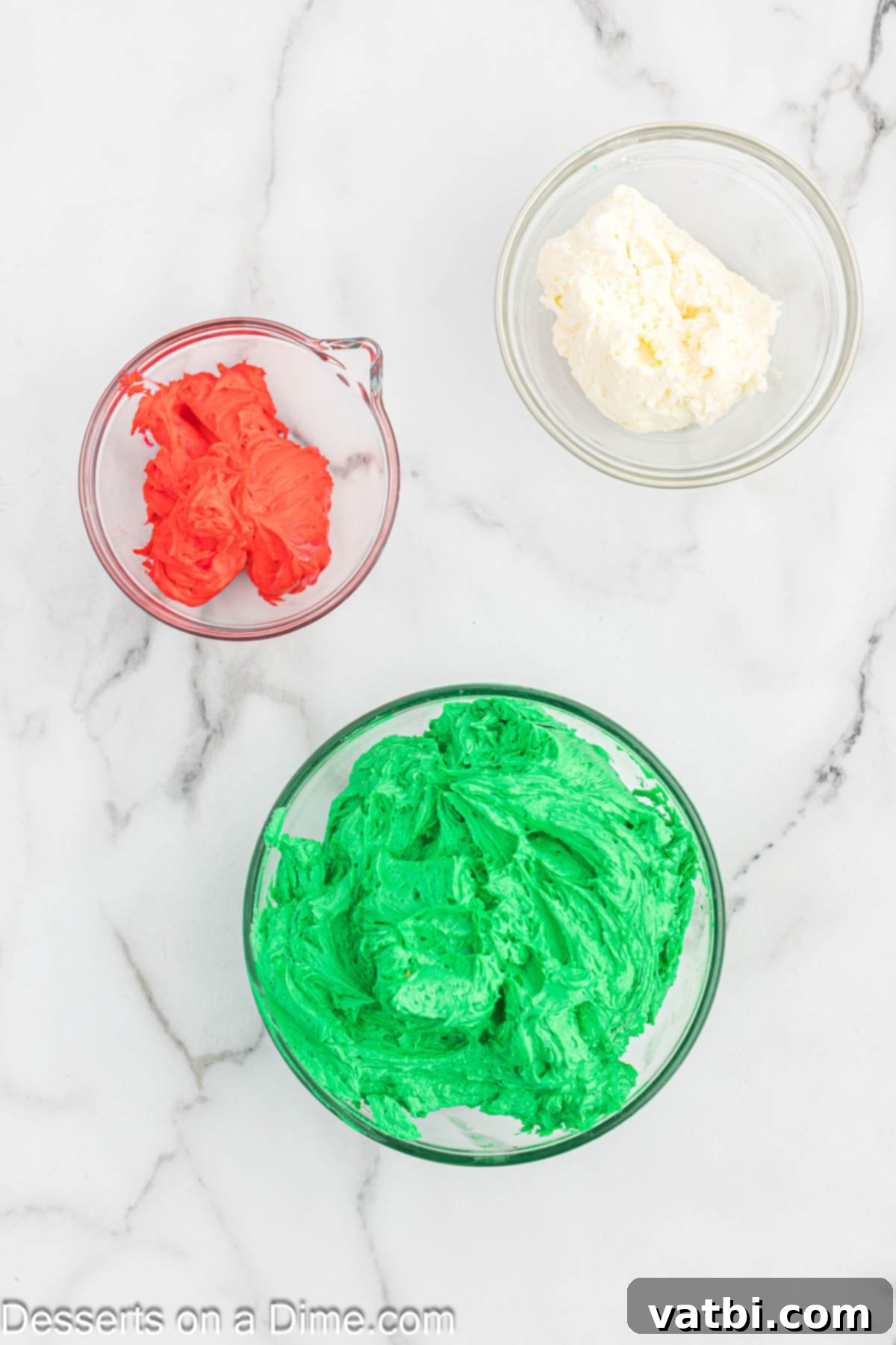 Three separate bowls filled with buttercream frosting in vibrant red, white, and green colors.