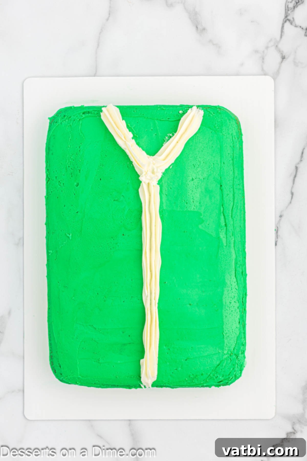 White frosting piped onto the green-frosted cake to create a V-neck shape and a thick vertical line down the middle.