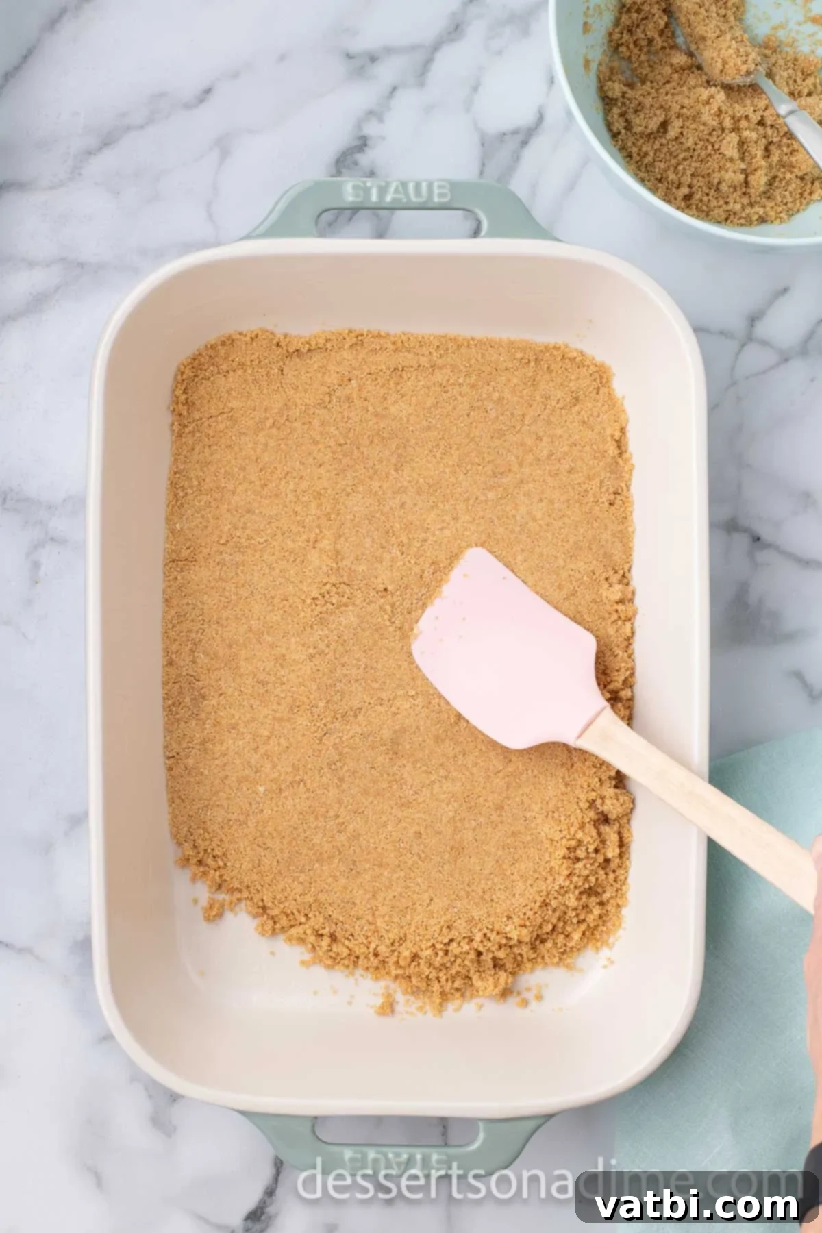Crimson Craving 5 Baking dish with graham cracker crumbs pressed into the bottom with a spatula.