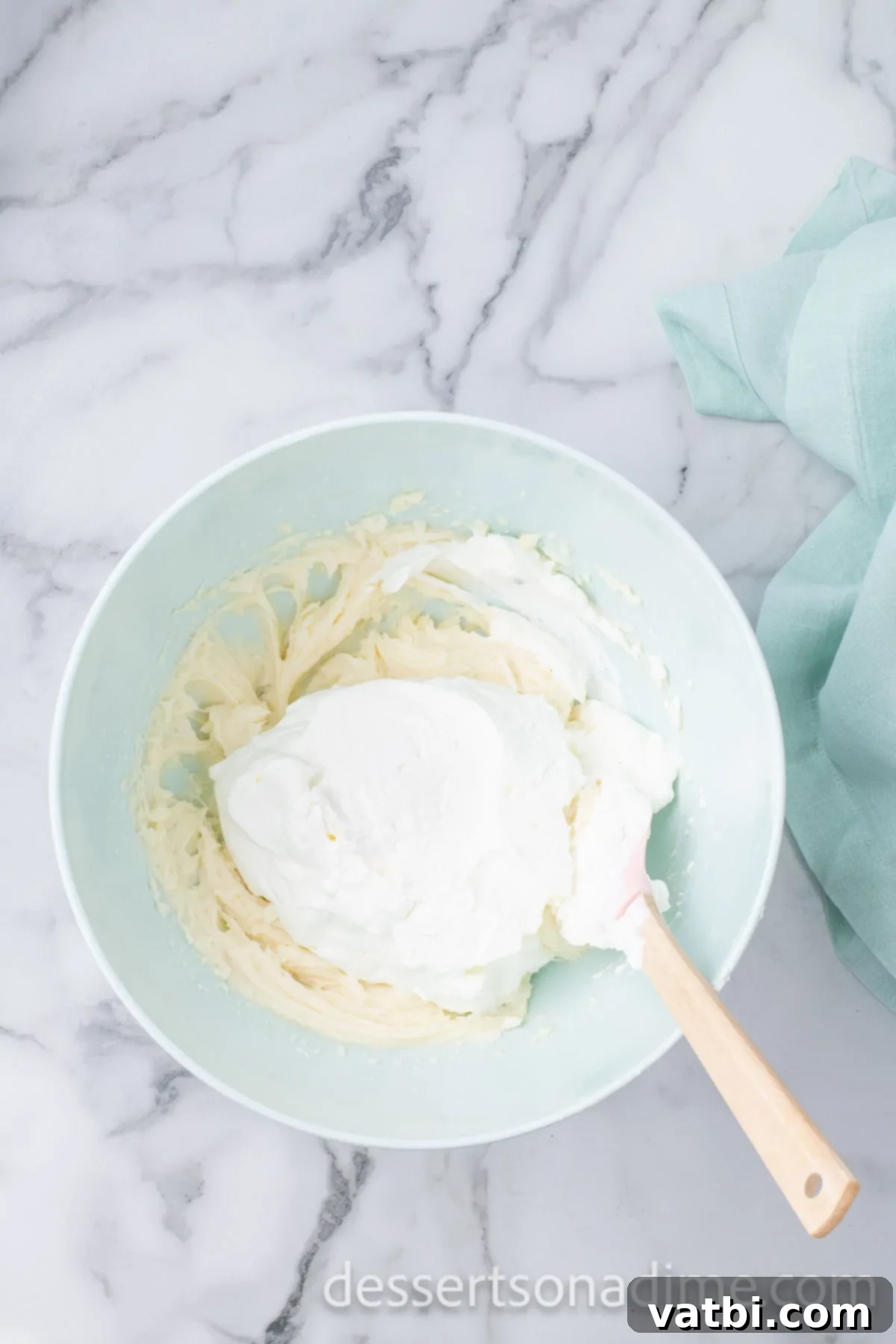 Crimson Craving 8 Mixing bowl combining whipped cream and cream cheese mixture with a spatula.