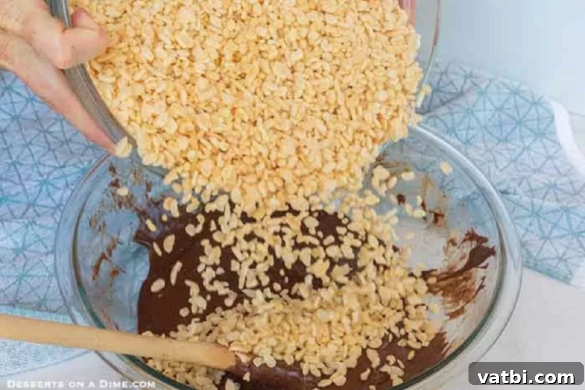 Decadent Chocolate Krispie Squares 3 Crispy rice cereal being poured into the melted chocolate and marshmallow mixture in a large bowl.