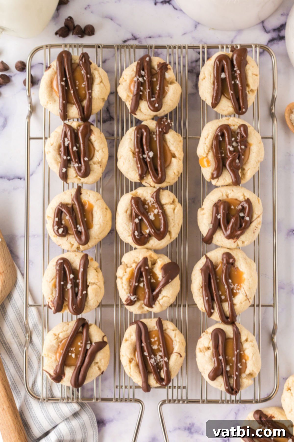 Twix Thumbprint Cookies cooling on a wire rack, topped with glossy chocolate and caramel, ready for a sprinkle of sea salt.
