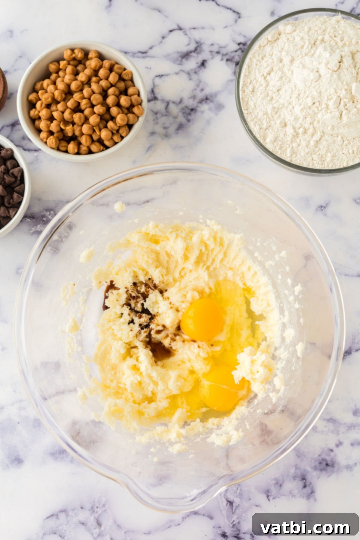 Room temperature eggs and vanilla extract being combined with the creamed butter and sugar mixture in a bowl.