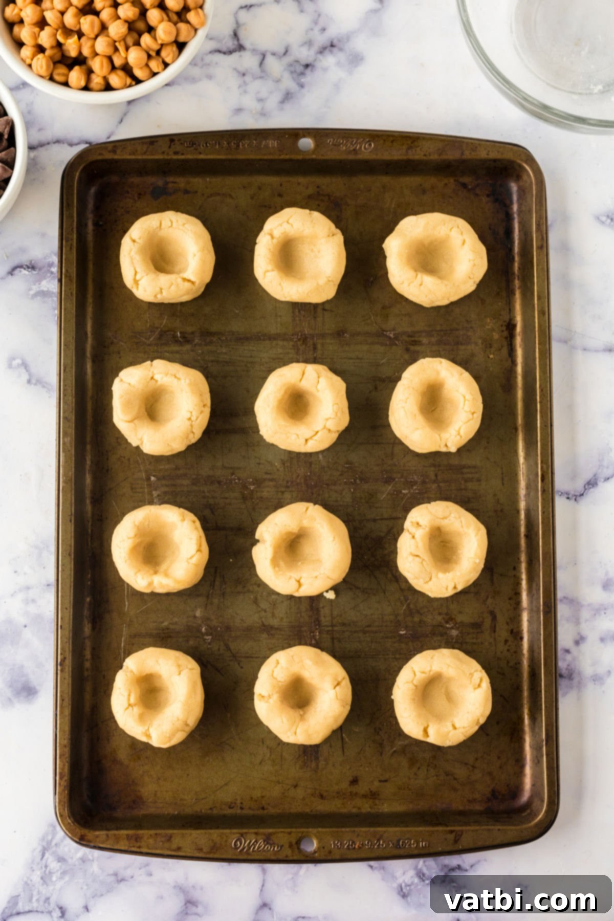 Cookie dough divided into uniform balls on a baking sheet, ready for the thumbprint indentation.