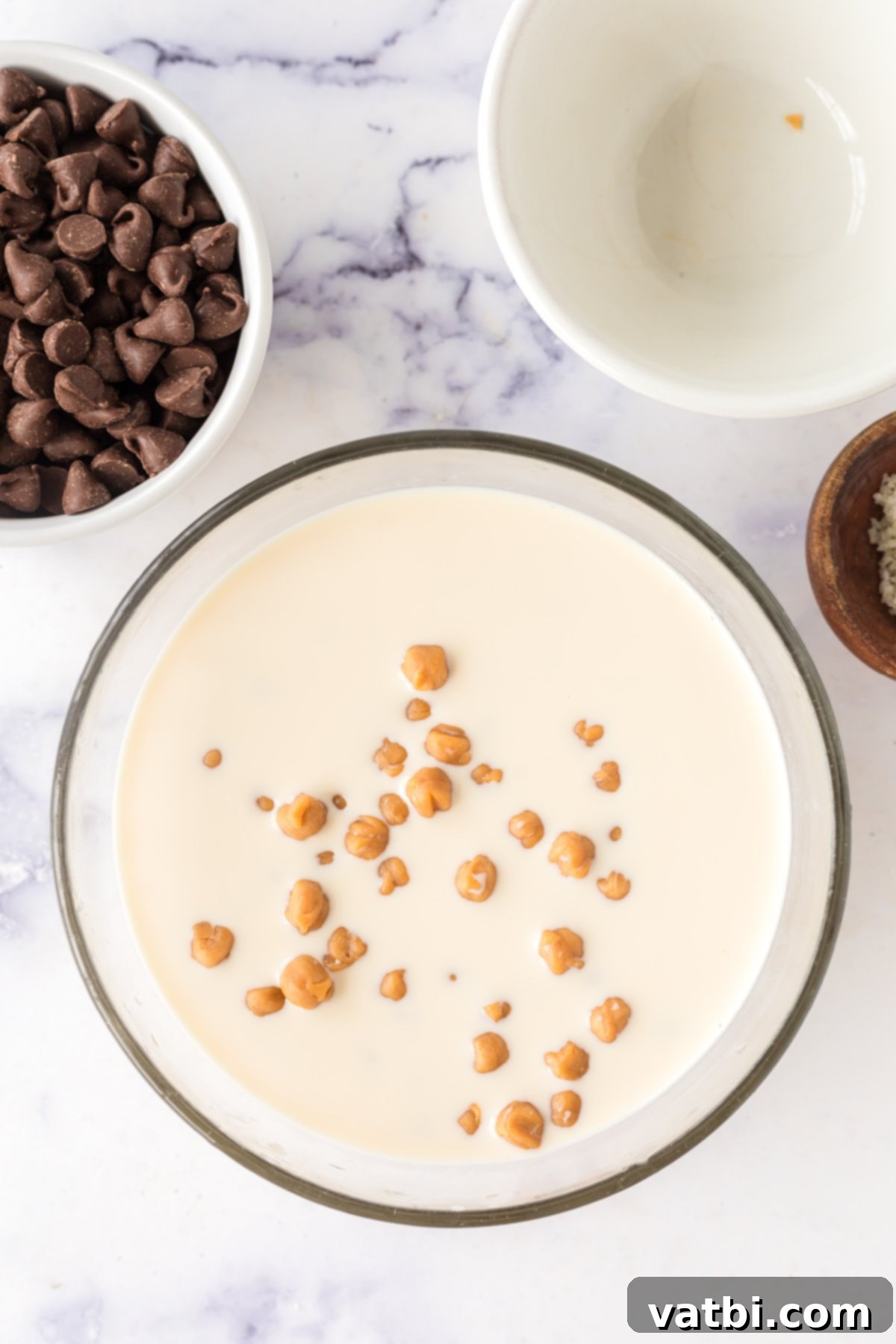 A mixing bowl with caramel bits and evaporated milk, melting together in the microwave to create a smooth caramel sauce.