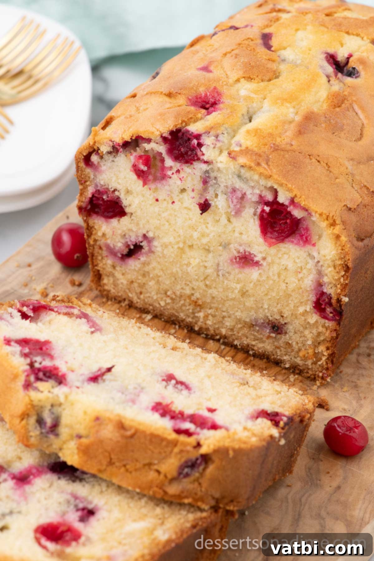 Loaf of cranberry bread being sliced, showing the moist texture and vibrant cranberries inside.