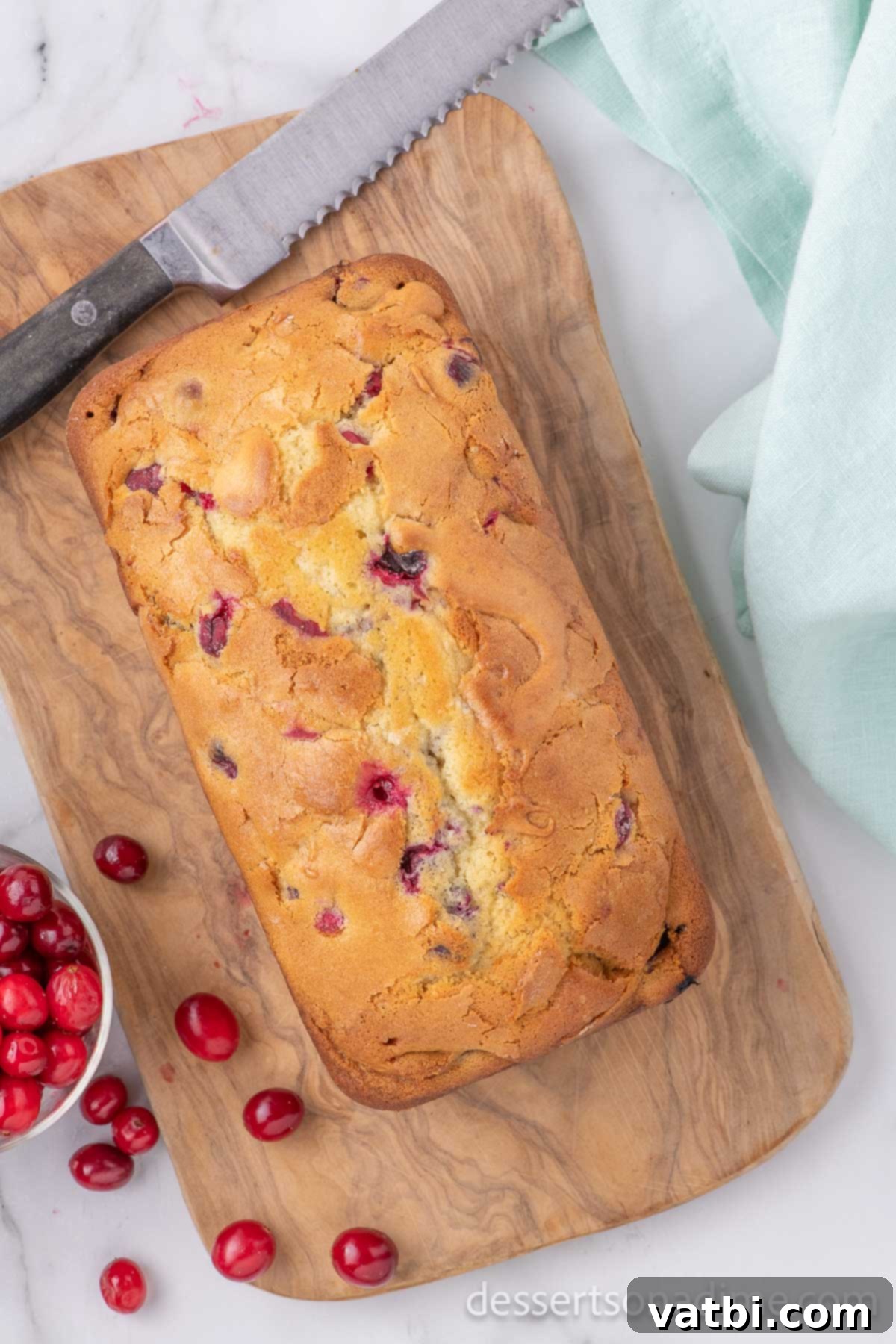 A freshly baked loaf of Cranberry Bread sitting on a wire rack, ready to be sliced.