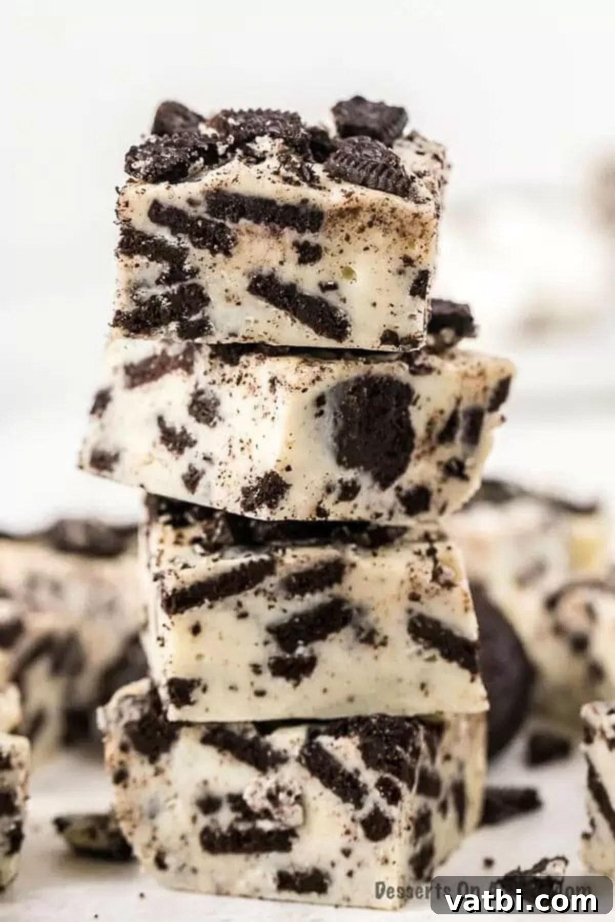Oreo fans will go crazy over this super easy 3 ingredient Oreo fudge recipe. Oreo fudge is so easy to make and delicious with white chocolate and sweetened condensed milk. Learn how to make oreo fudge with this no bake three ingredient recipe. #dessertonadime #oreofudgerecipe Oreo Fudge cut into squares and stacked, showcasing the creamy texture and cookie pieces.