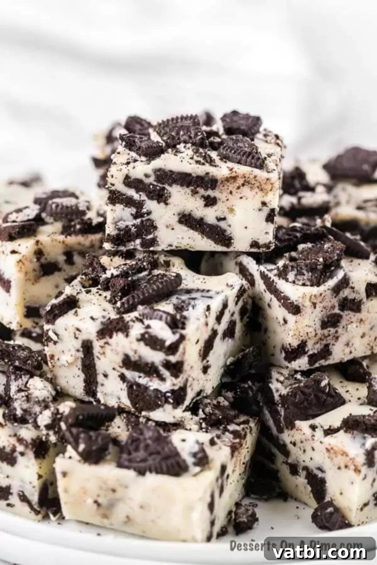 Oreo fans will go crazy over this super easy 3 ingredient Oreo fudge recipe. Oreo fudge is so easy to make and delicious with white chocolate and sweetened condensed milk. Learn how to make oreo fudge with this no bake three ingredient recipe. #dessertonadime #oreofudgerecipe Oreo fudge cut into a square and then stacked on a plate, ready to be served.