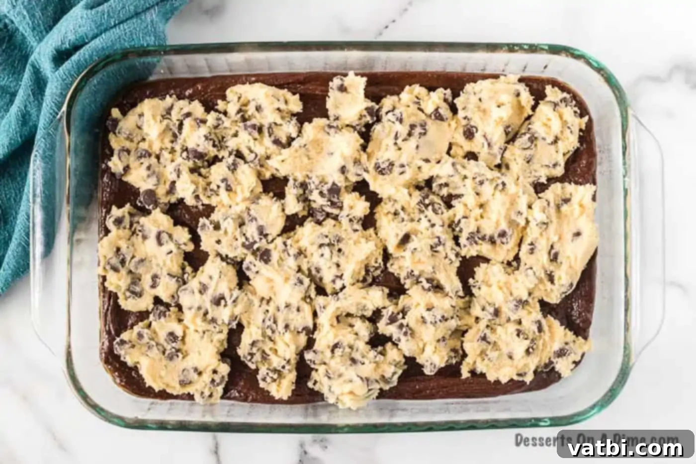 Dollops of chocolate chip cookie dough placed on top of brownie batter in a baking pan.