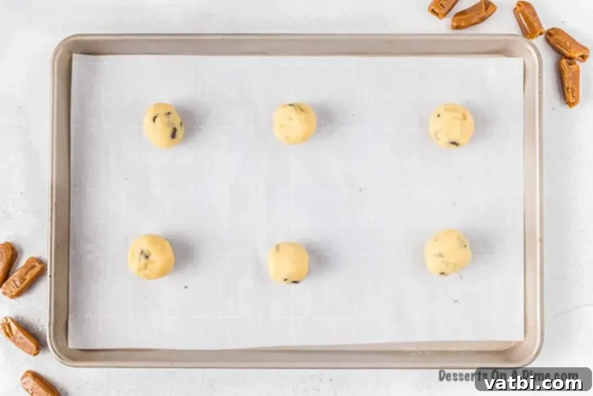 Scoops of cookie dough arranged neatly on a parchment-lined baking sheet, spaced out for chilling.