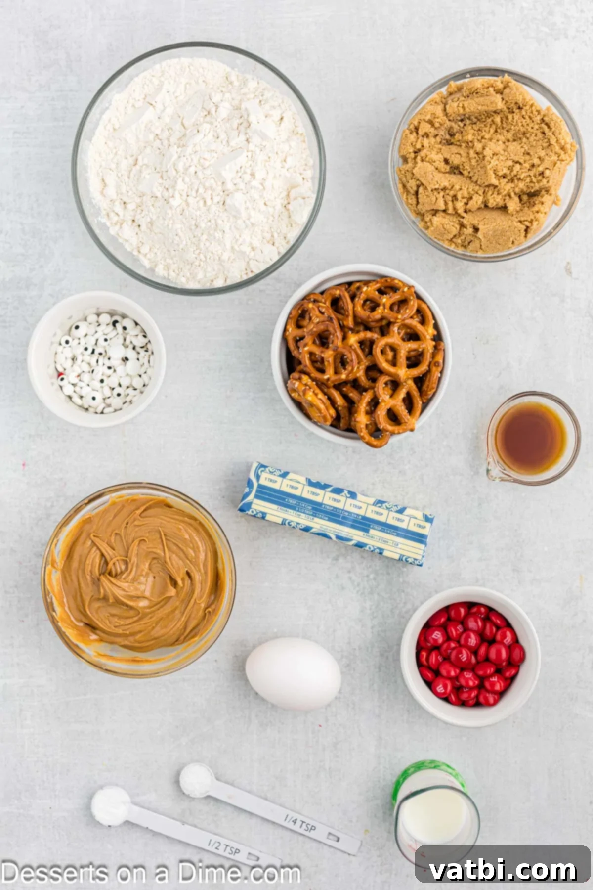 Holiday Reindeer Delights 3 A flat lay image displaying all the ingredients for Reindeer Cookies: flour, brown sugar, candy eyes, pretzels, creamy peanut butter, red M&M's, and an egg.