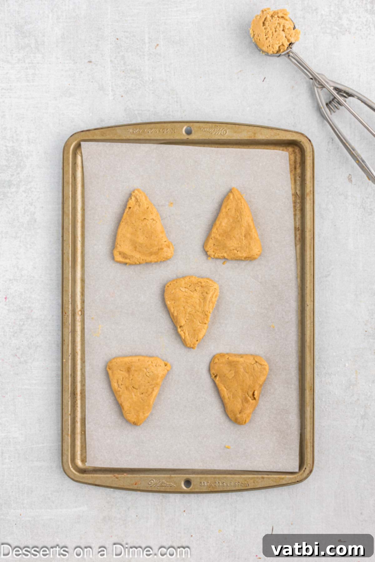 Holiday Reindeer Delights 7 Cookie dough balls shaped into triangles on a baking sheet, ready for the oven.