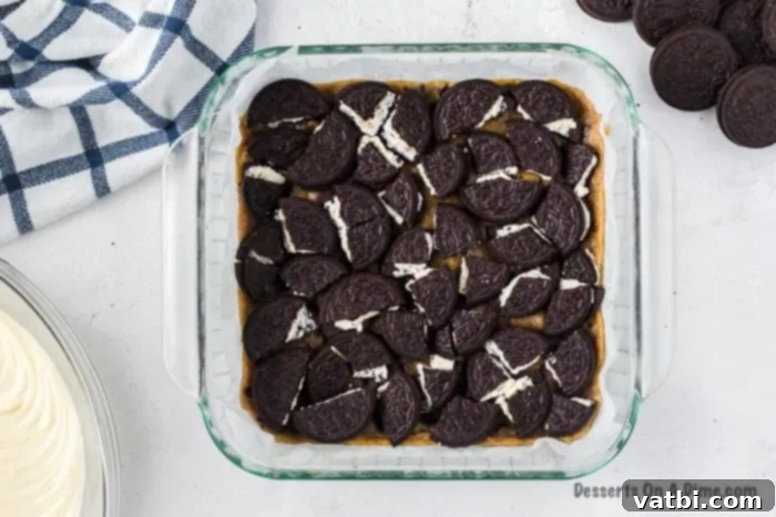 Decadent Loaded Cheesecake Bars 4 A single layer of Oreo cookies arranged on top of the baked chocolate chip cookie dough crust in a baking dish.