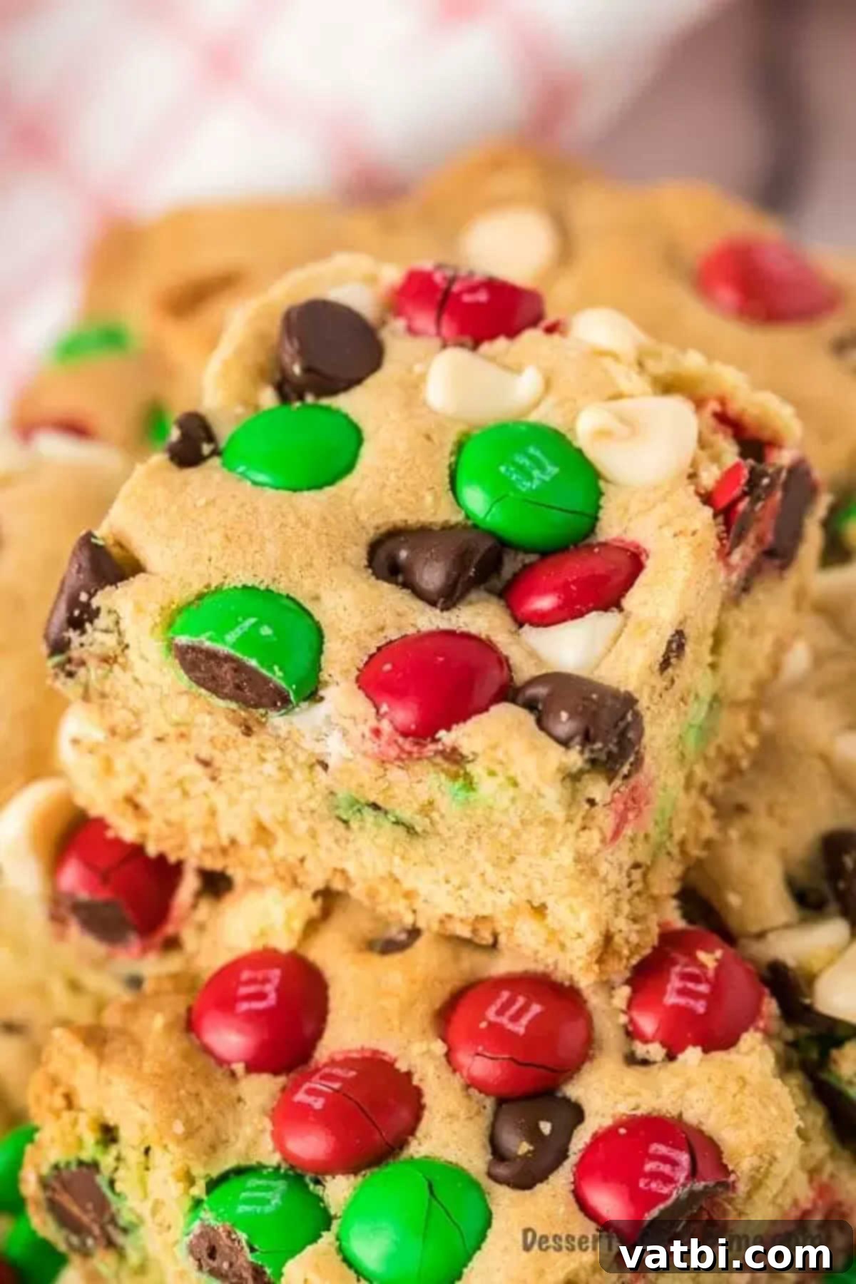 Christmas cookie bars are packed with chocolate chips, M&M's and more to make this easy recipe amazing. Each bite of this chewy chocolate chip recipe is so ooey gooey for a decadent treat. Try these lazy M&M cookie bars for the holidays. #dessertonadime #christmascookiebars #M&M #Mm #Chocolatechip #gooeychocolatechip Stacked Christmas chocolate chip cookie bars with M&M's, showcasing their gooey interior and festive colors.