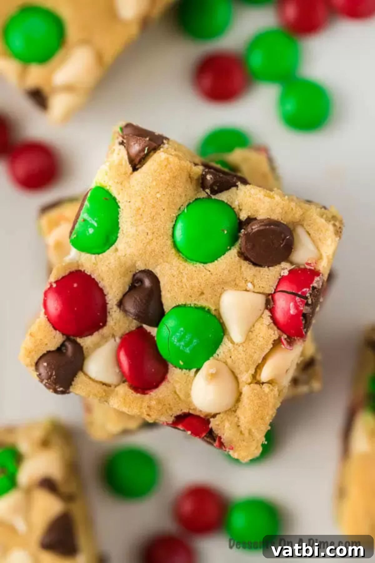 Christmas cookie bars are packed with chocolate chips, M&M's and more to make this easy recipe amazing. Each bite of this chewy chocolate chip recipe is so ooey gooey for a decadent treat. Try these lazy M&M cookie bars for the holidays. #dessertonadime #christmascookiebars #M&M #Mm #Chocolatechip #gooeychocolatechip Close-up of a stack of Christmas chocolate chip cookie bars, showing the gooey chocolate and colorful M&M's.