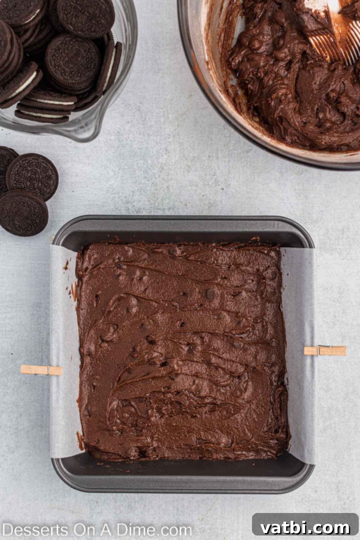 Decadent Oreo Brownies 5 Approximately half of the rich, chocolate brownie batter is spread evenly into the parchment-lined baking dish, forming the base layer.