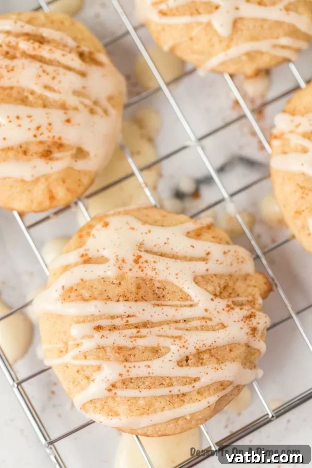 A single frosted eggnog cookie cooling on a rack, awaiting its place at the holiday party. A single eggnog cookie with glaze on a wire cooling rack, with more blurred cookies in the background.