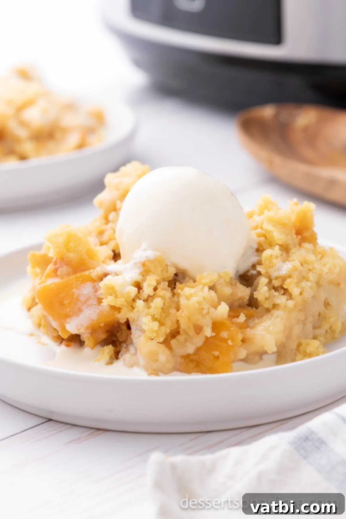 Effortless Slow Cooker Peach Delight 9 Peach Dump Cake in a bowl with vanilla ice cream.