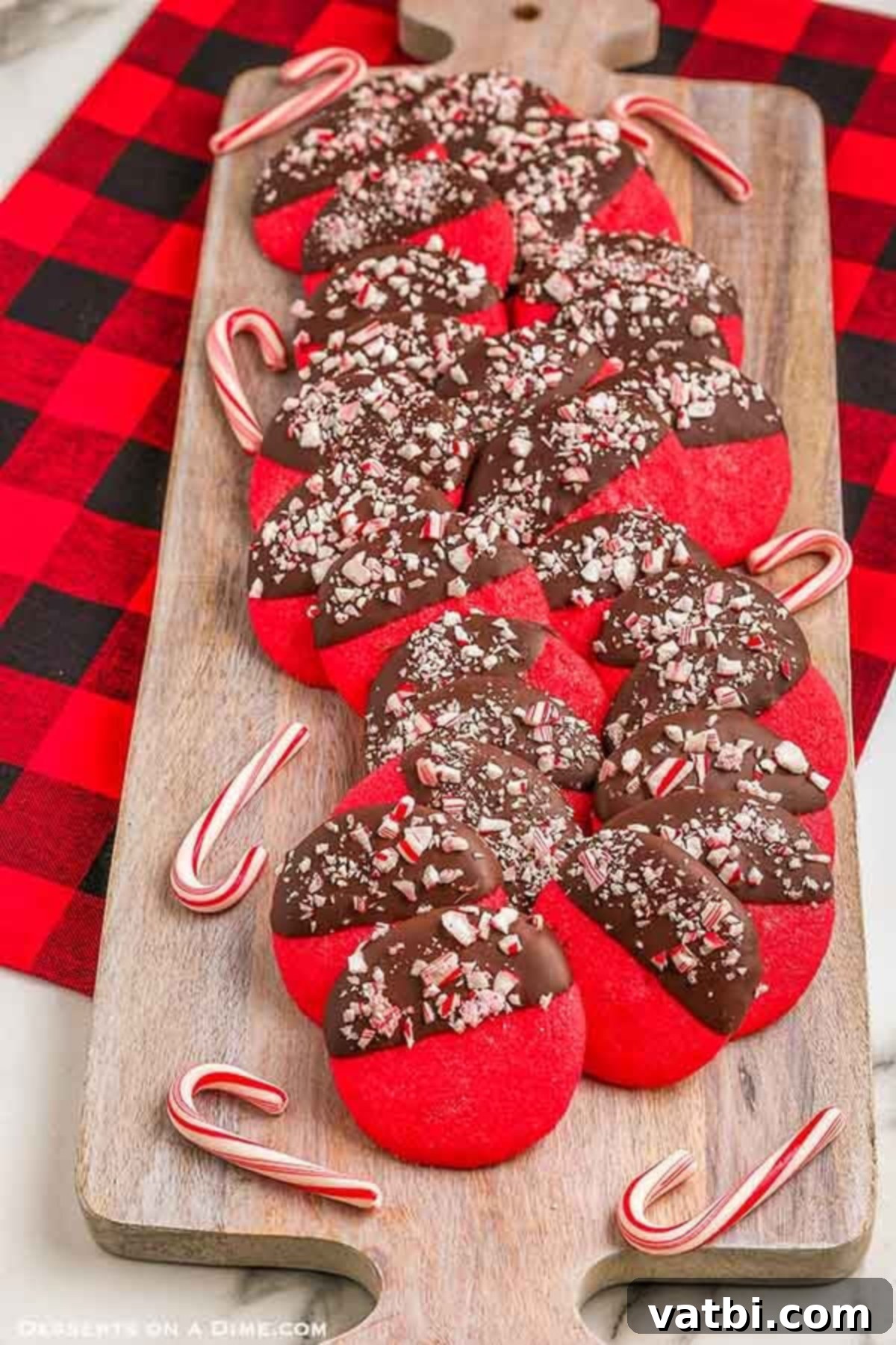 Chocolate dipped peppermint cookies look festive with the peppermint and chocolate combination. Make Peppermint cookies dipped in chocolate a Christmas tradition! Red peppermint cookies are easy to make and everyone will love the chocolate dipped cookie with crushed candy cane. This easy recipe for peppermint cookies is the best and the dough is easy to make. #dessertonadime #chocolatepeppermintcookies #cocoa Chocolate Dipped Peppermint Cookies on a wooden board. Festive and delicious, perfect for the holidays.