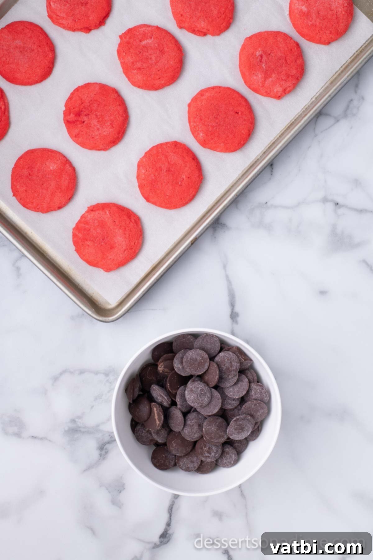 Dipped Peppermint Chocolate Delights 11 Cookies on baking sheet beside a bowl of chocolate. Cooled cookies on a wire rack.