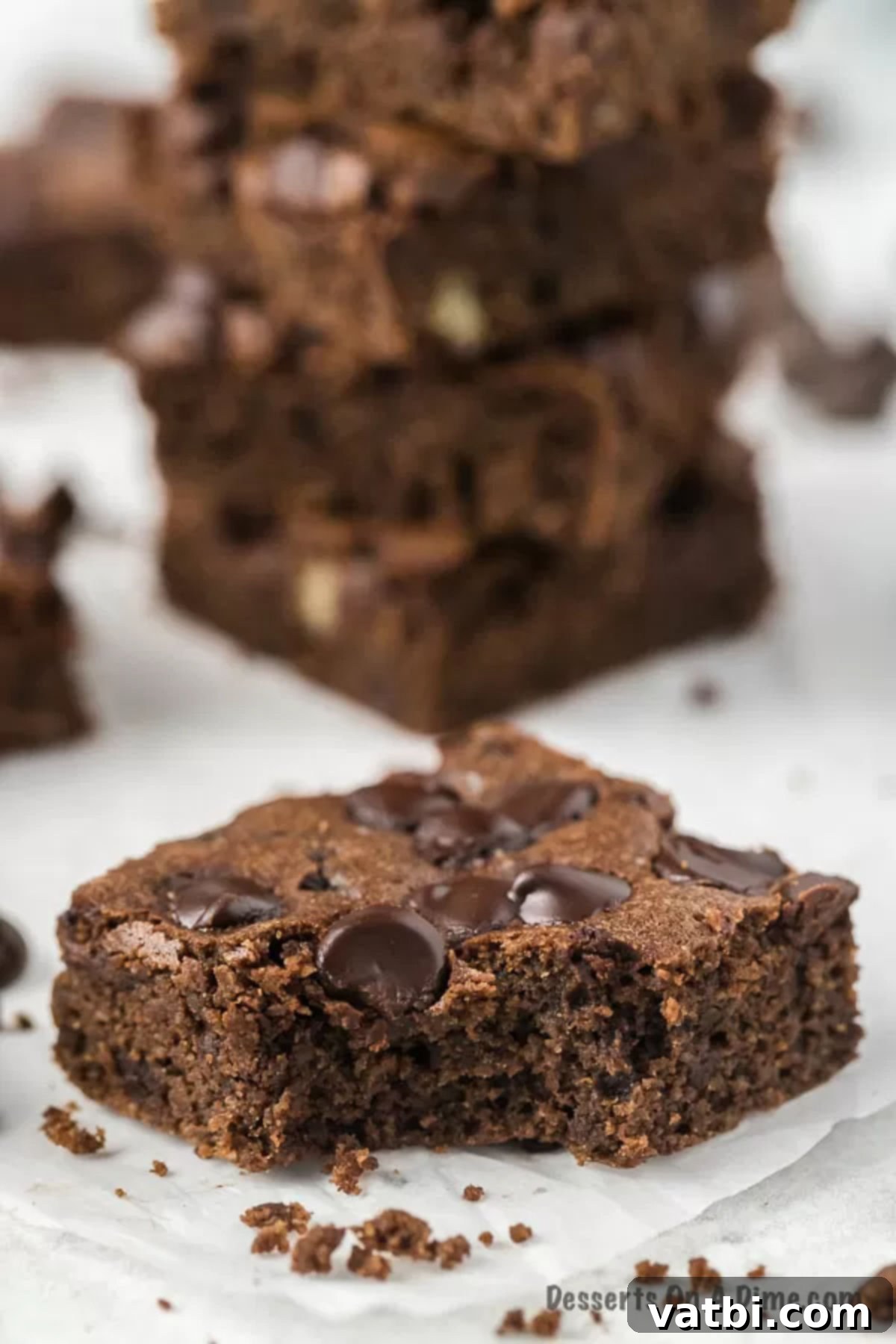 Keto brownies are so delicious and such an easy low carb treat that everyone will enjoy. This easy recipe makes the best fudgy gooey brownies with cocoa powder. Try this simple and healthy easy low carb chocolate brownie recipe with almond flour. The worlds best easy fudgy chewy brownie with just a few ingredients. #dessertonadime #ketobrownies #easyalmondflour #ketobrownieseasy #recipes Stack of four Keto Brownies, showing their thick, fudgy center and topping of chocolate chips, on a rustic wooden surface.