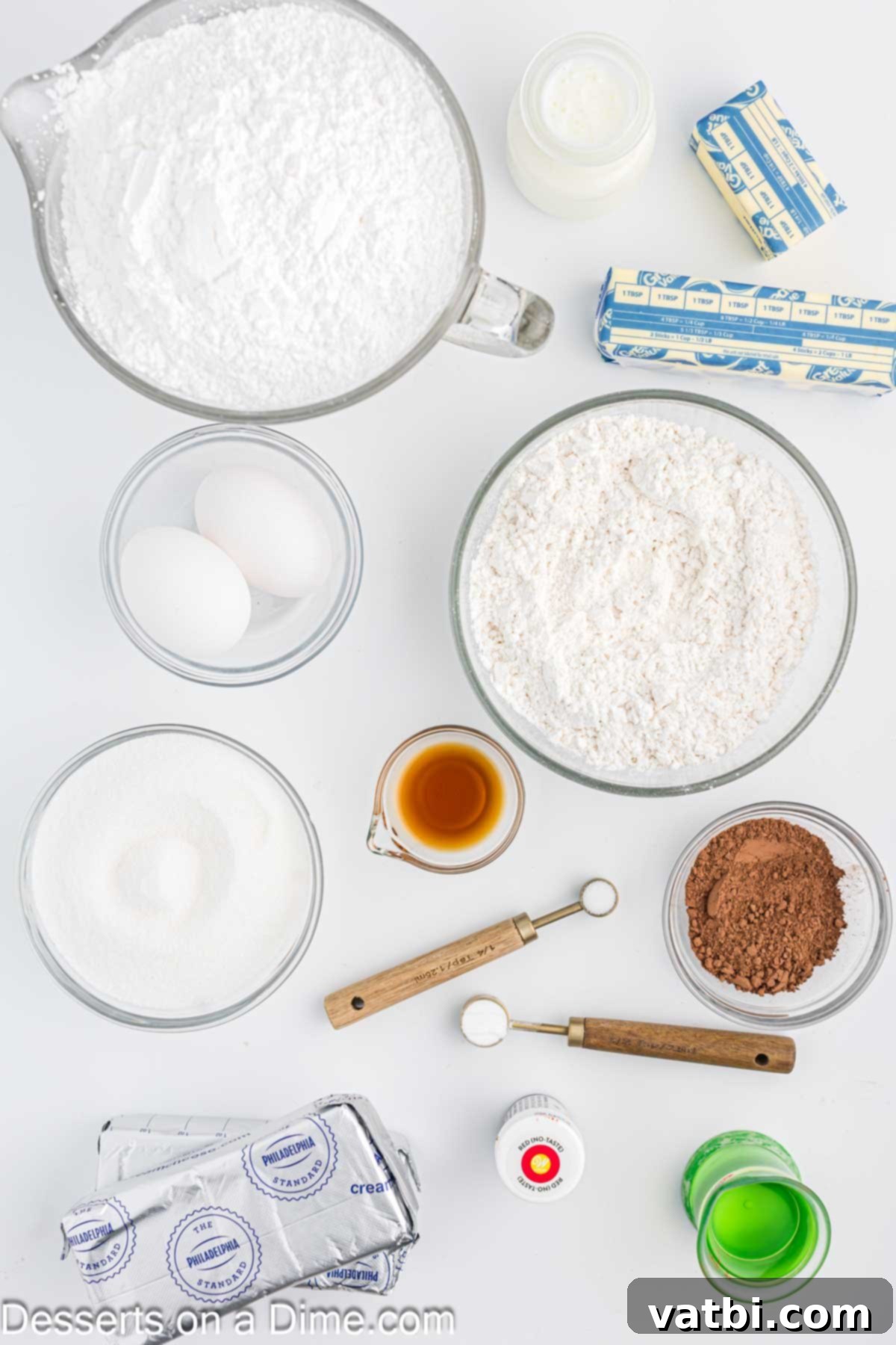 Assortment of red velvet cupcake ingredients including cake flour, cocoa powder, baking soda, eggs, vanilla extract, red food coloring, buttermilk, cream cheese, butter, and powdered sugar, neatly arranged for baking.
