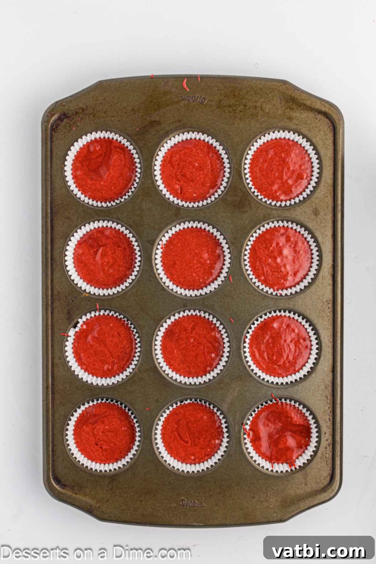 Red velvet cupcake batter poured evenly into muffin tins lined with paper liners.