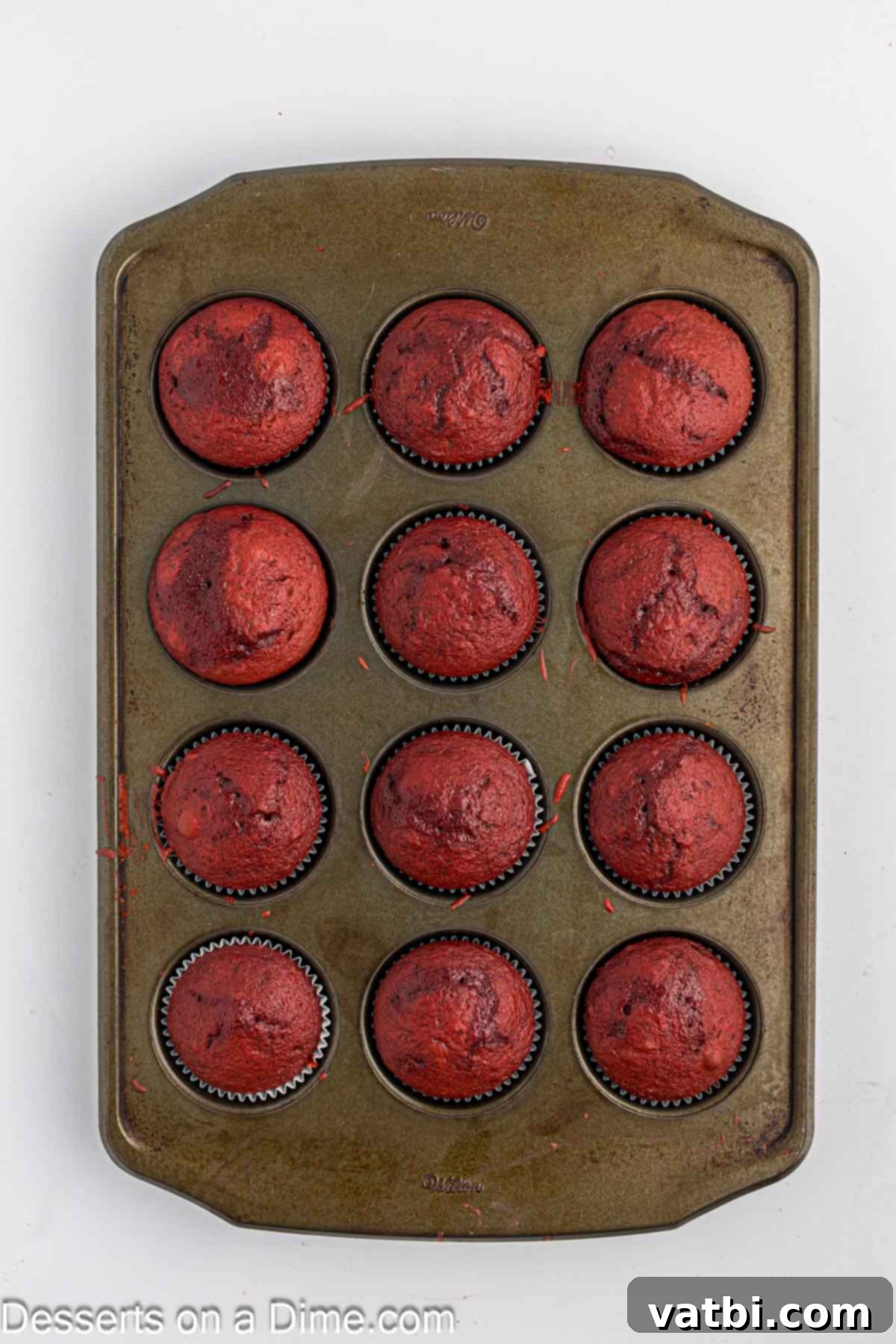 Freshly baked red velvet cupcakes in a muffin pan, golden brown around the edges.