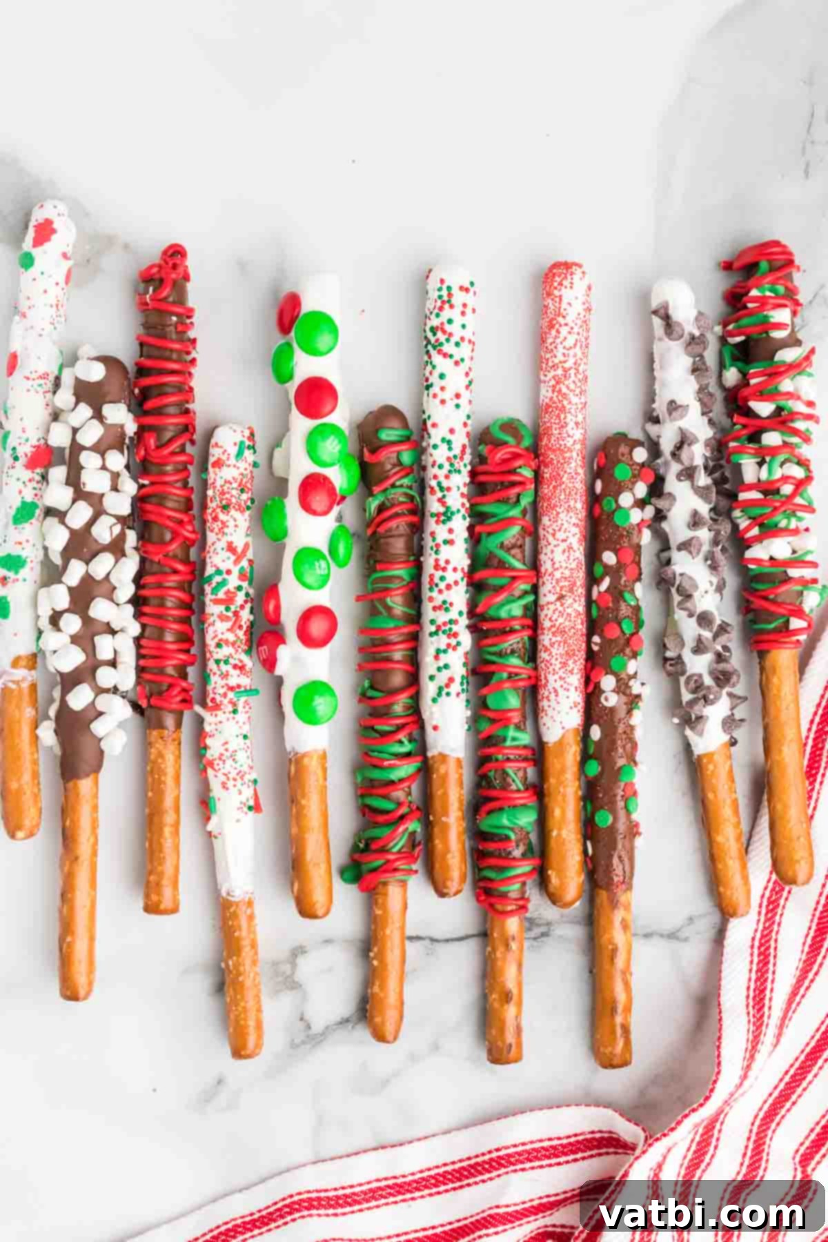 Homemade Christmas Chocolate Covered Pretzel Rods: An easy, tasty, and fun DIY holiday treat perfect for gifts or parties. Learn to make this festive chocolate-dipped pretzel recipe today! Pretzel Rods dipped in colorful Christmas chocolate and adorned with festive sprinkles, M&Ms, and crushed candy canes for a holiday treat