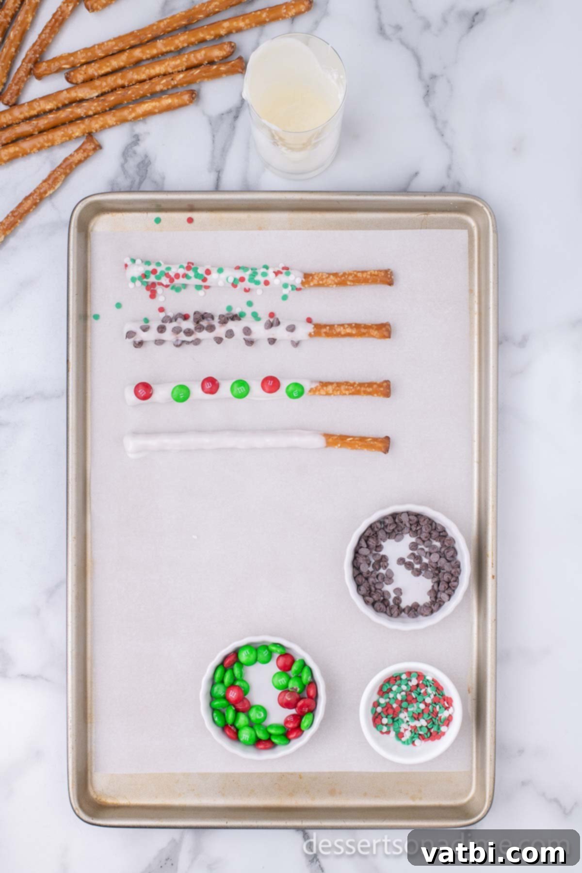 Sweet & Salty Holiday Pretzel Treats 3 Freshly dipped pretzel rods on a parchment-lined baking sheet, ready for toppings