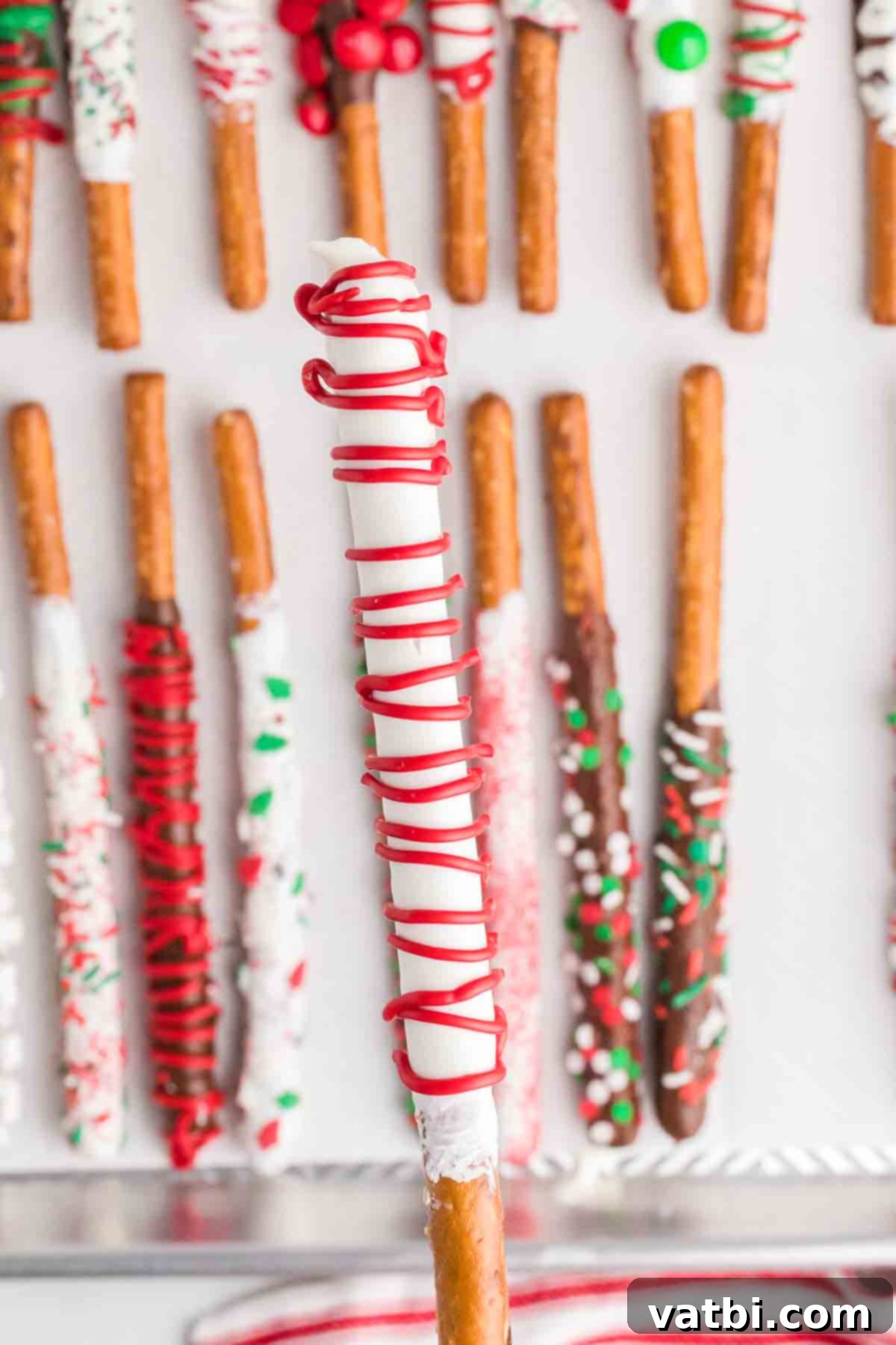 Homemade Christmas Chocolate Covered Pretzel Rods: An easy, tasty, and fun DIY holiday treat perfect for gifts or parties. Learn to make this festive chocolate-dipped pretzel recipe today! Close-up of a perfectly decorated Chocolate Covered Pretzel Rod with red candy melt drizzle and festive sprinkles