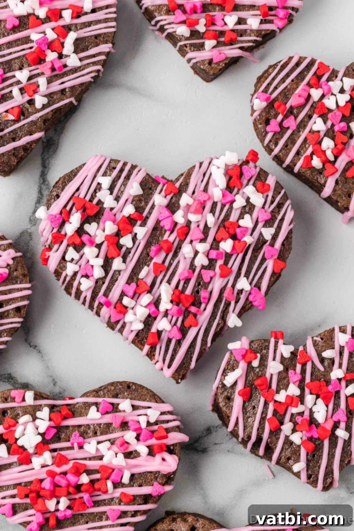 Sweetheart Brownie Delights 2 Brownies cut into hearts, glistening with a chocolatey sheen and adorned with colorful sprinkles, sitting on a parchment-lined tray.
