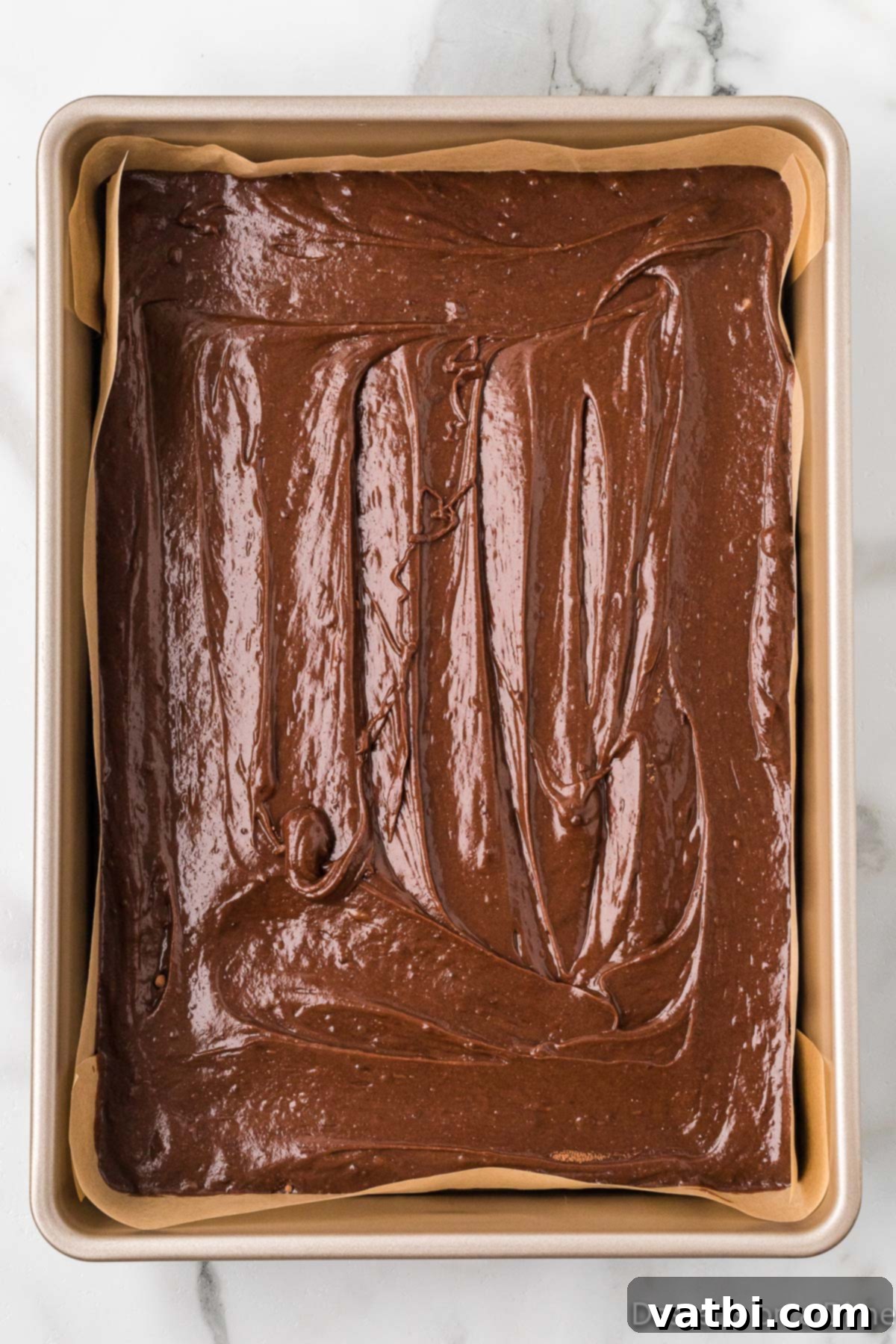 Sweetheart Brownie Delights 6 Smooth, dark brownie batter evenly spread in a parchment-lined 9x13 inch baking pan, ready for baking.