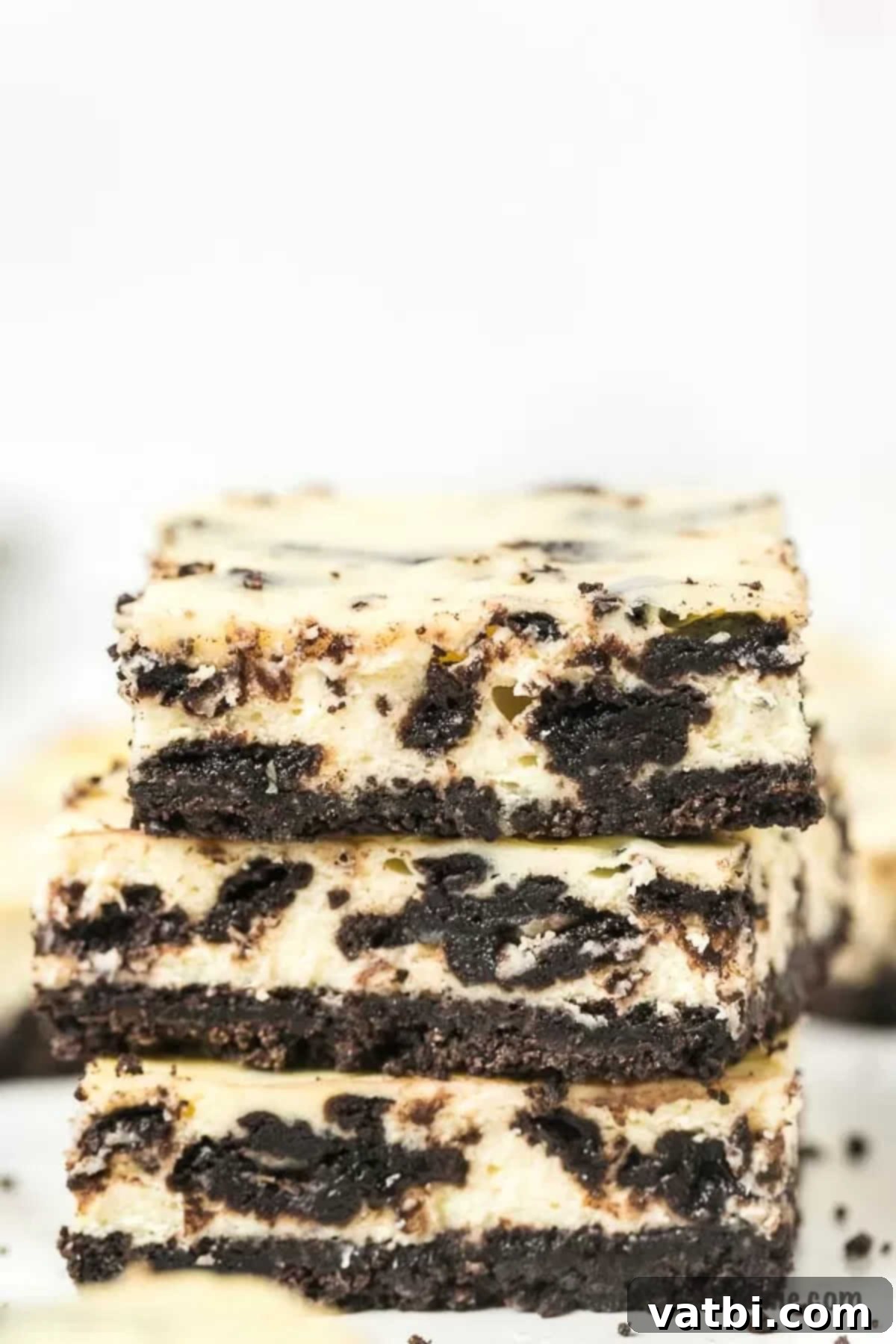 Irresistible Oreo Cheesecake Delight 2 Three decadent Oreo Cheesecake Bars stacked artfully, showcasing the dark cookie crust and creamy white cheesecake filling with crushed Oreo pieces.
