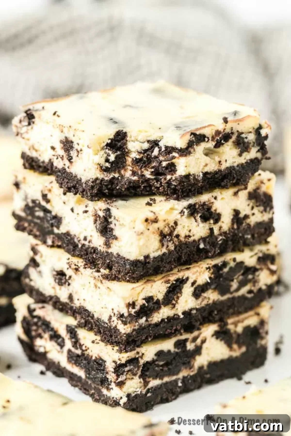 Irresistible Oreo Cheesecake Delight 16 Four Oreo Cheesecake Bars stacked, with one bar showing a delicious bite taken out of it, revealing the creamy filling and cookie pieces.