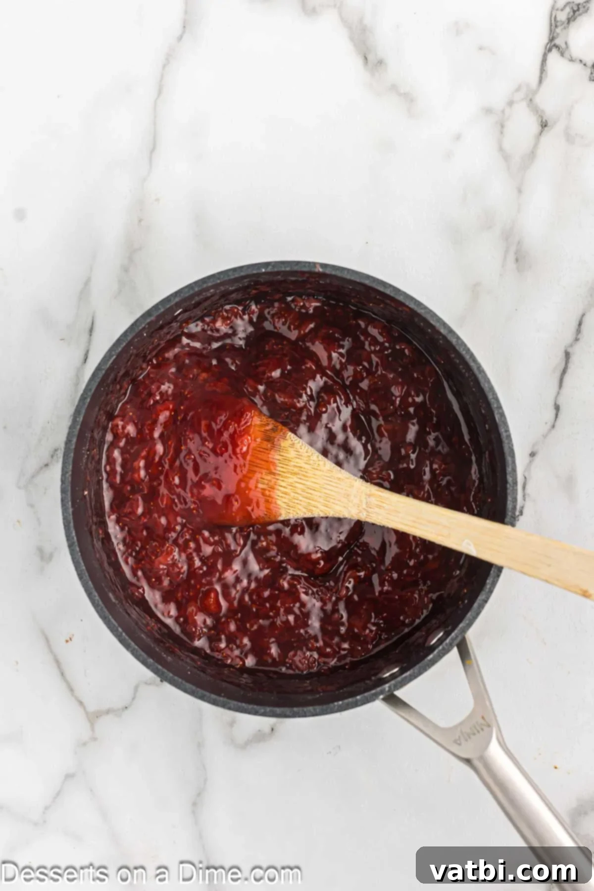 Thickened strawberry sauce in a pan with mashed strawberry pieces.