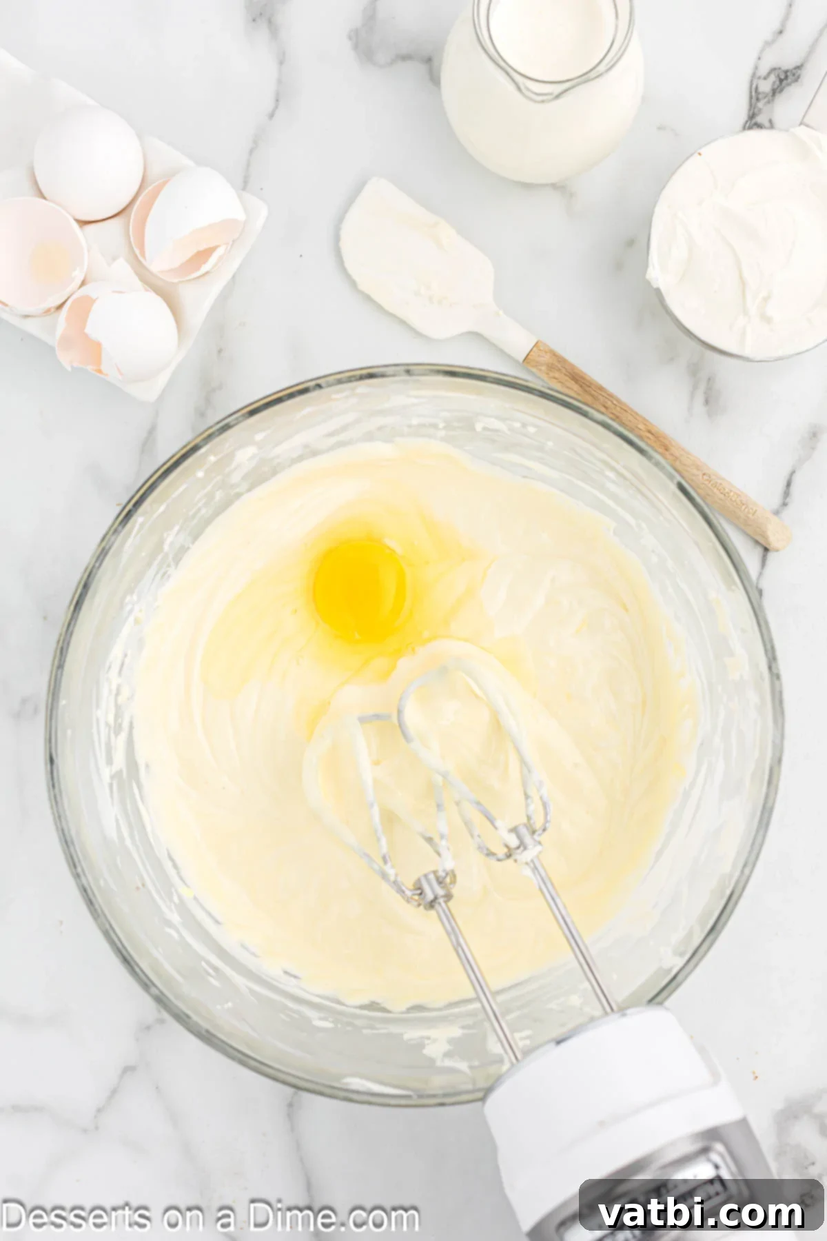 Eggs being added one at a time to the cream cheese mixture in a bowl.