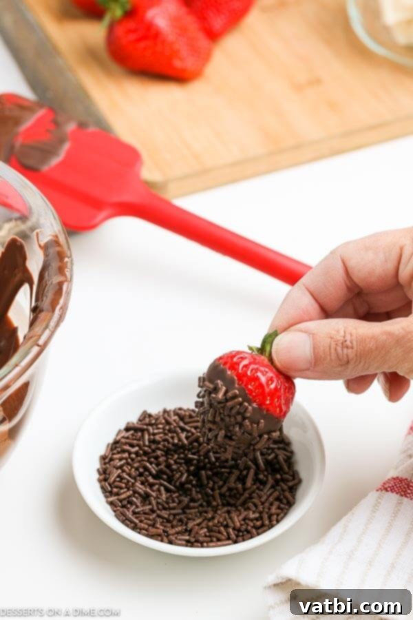 Decadent Strawberry Delights 3 A fresh strawberry being dipped into a bowl of sprinkles after being coated in chocolate.