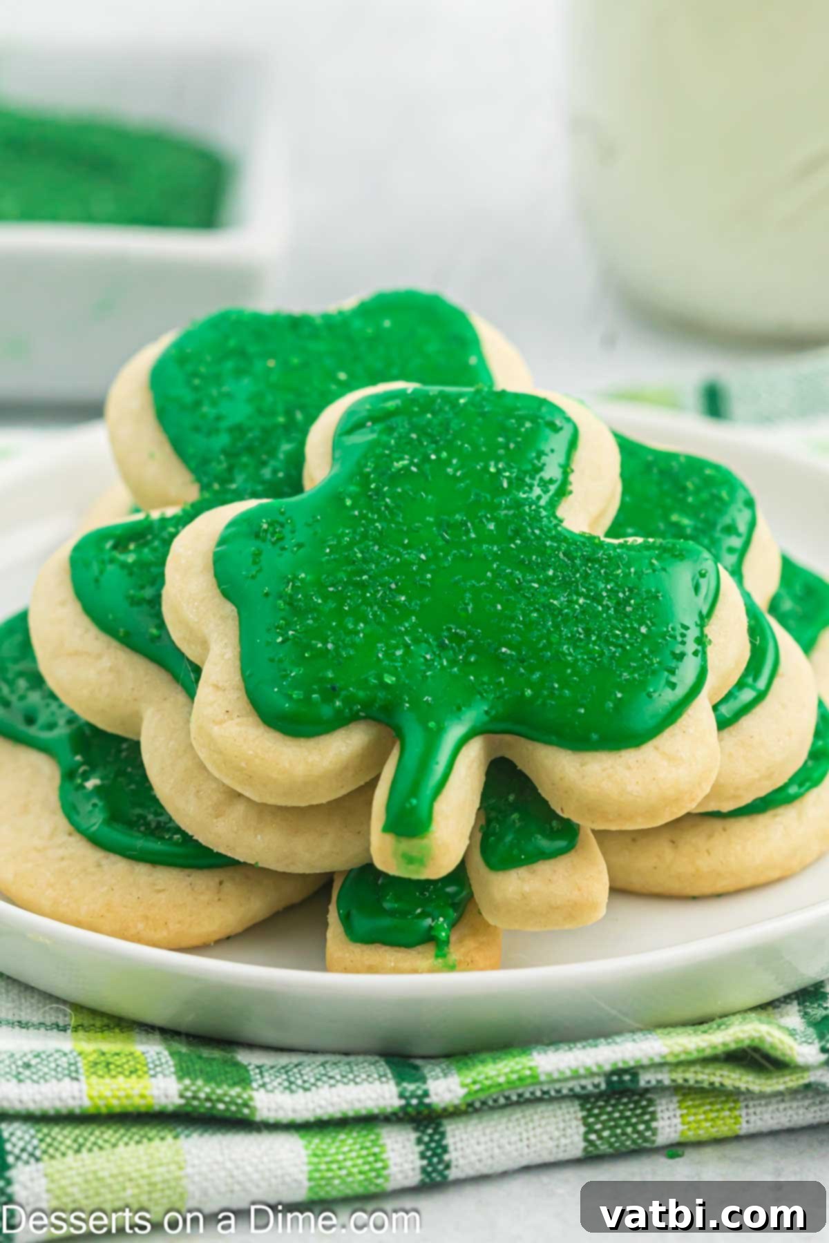 Sweet Clover Delights 16 A close-up of a plate brimming with freshly baked and decorated shamrock sugar cookies, showcasing their vibrant green frosting and sparkling sprinkles.
