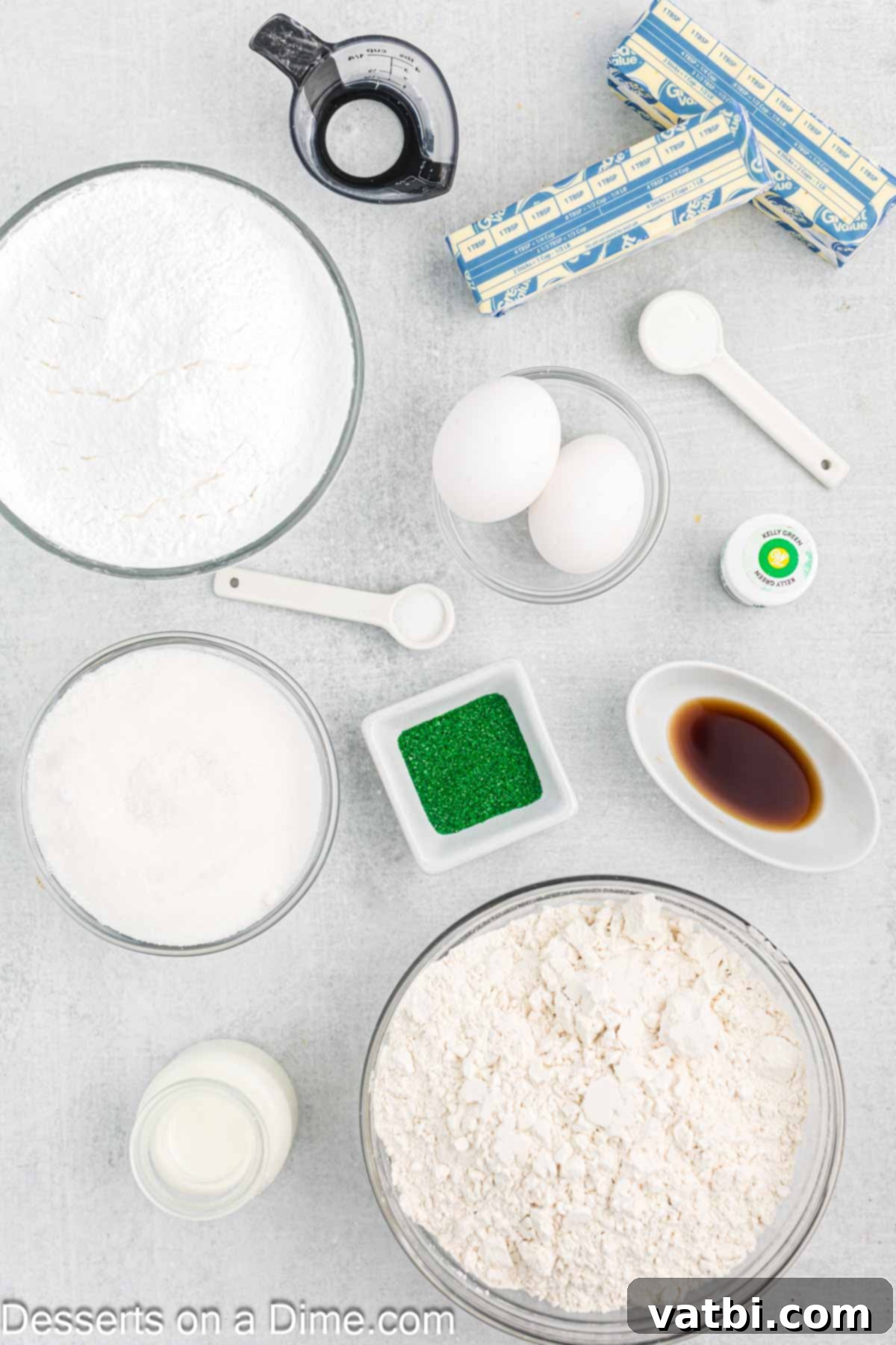 Sweet Clover Delights 3 A flat lay of all the essential ingredients for making Shamrock Cookies, including flour, butter, sugar, vanilla, eggs, baking powder, milk, powdered sugar, corn syrup, vivid green gel food coloring, and a variety of festive green sprinkles.