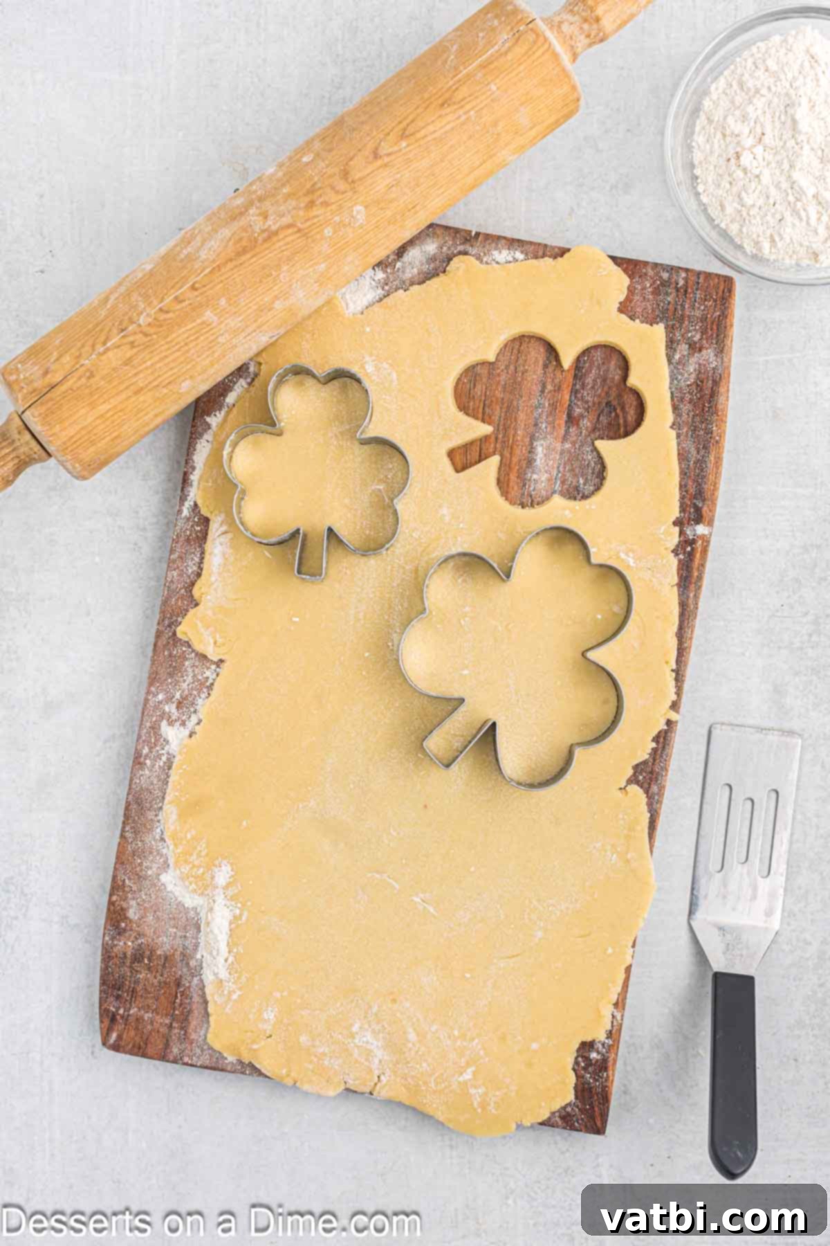 Sweet Clover Delights 8 Shamrock-shaped cookie dough cutouts arranged on a lightly floured surface, ready for transfer to a baking sheet.