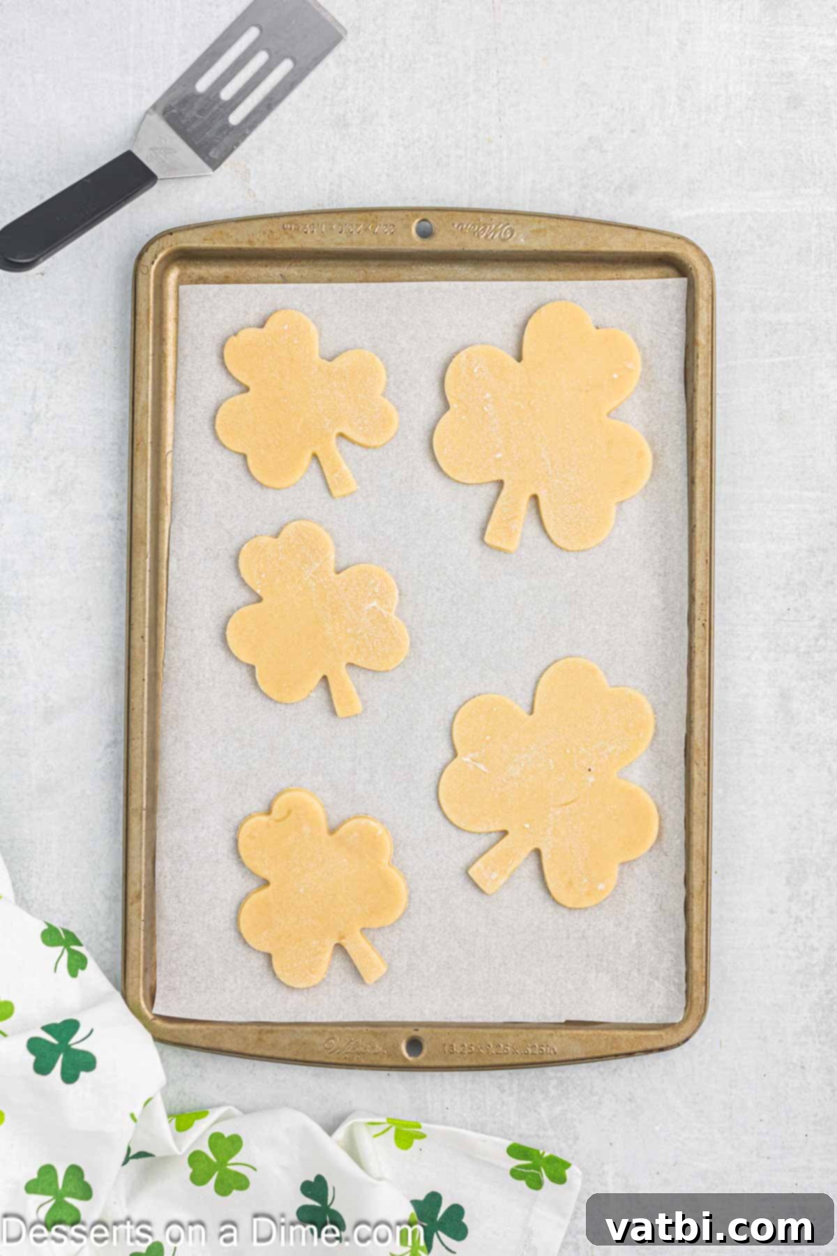 Sweet Clover Delights 9 Unbaked shamrock cookies neatly placed on a baking sheet lined with parchment paper, ready to go into the oven.