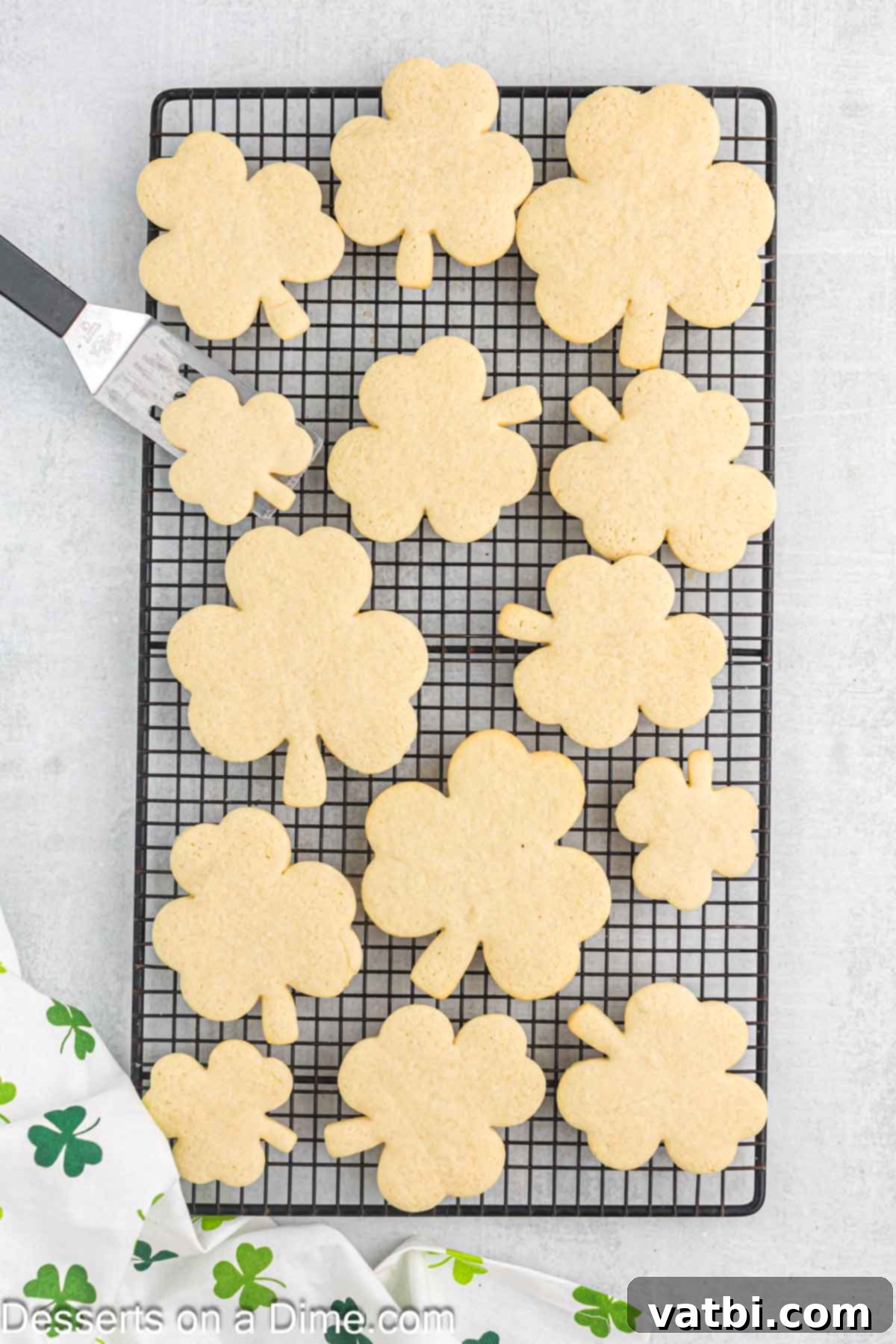 Sweet Clover Delights 10 Freshly baked shamrock cookies cooling on a wire rack, allowing air circulation for even cooling before frosting.