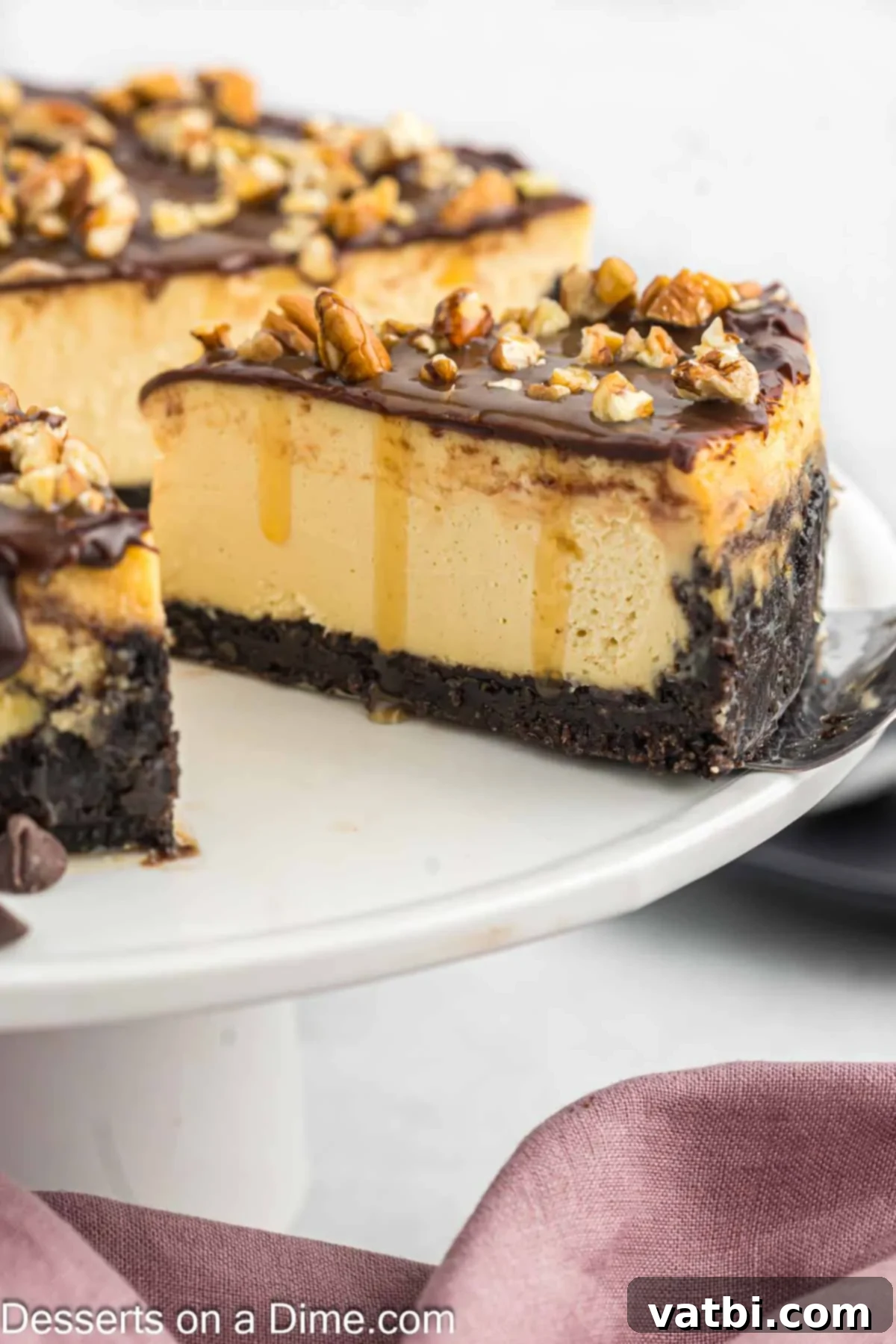 Turtle Cheesecake 2 A beautiful slice of Turtle Cheesecake showing its distinct layers: a dark Oreo crust, a thick creamy cheesecake filling, and a generous topping of golden caramel, rich chocolate drizzle, and chopped pecans. The slice is sitting on a white plate with a fork.