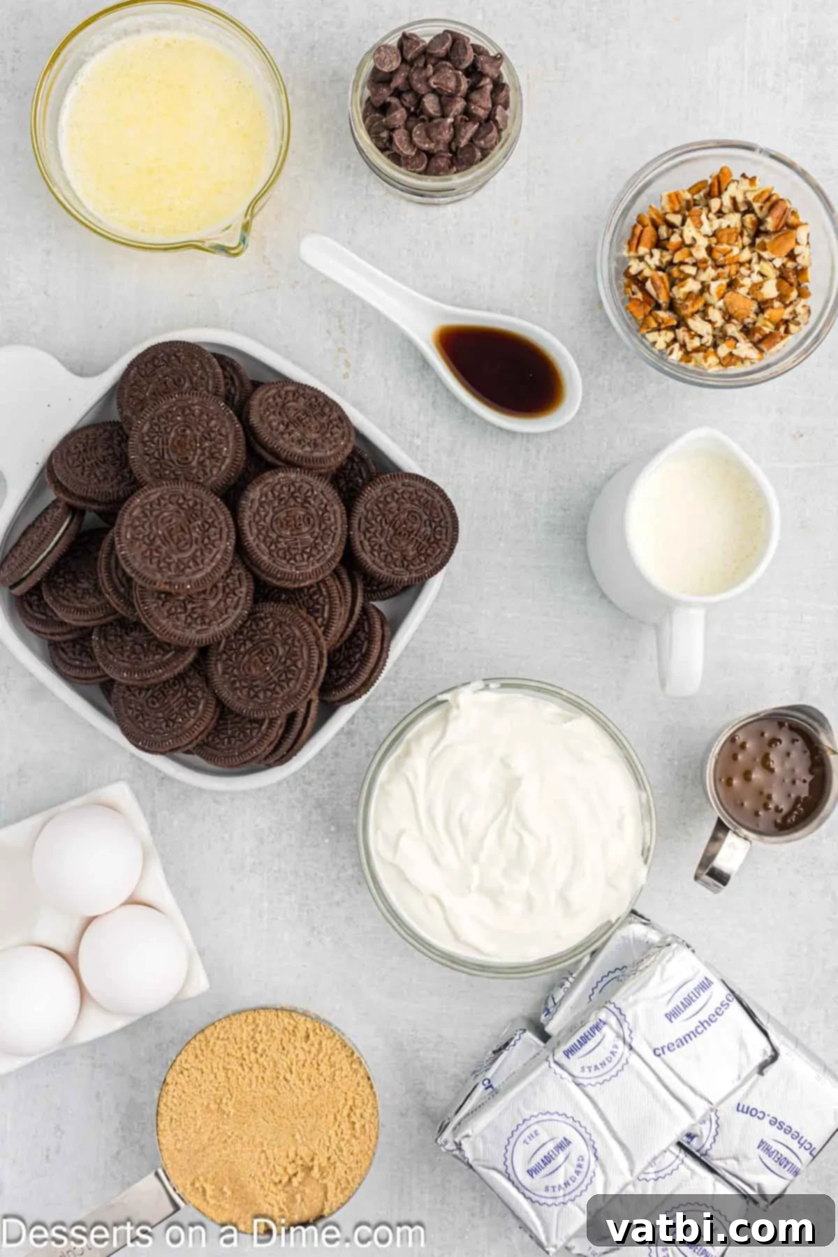 Turtle Cheesecake 3 A flat lay photograph showcasing all the fresh ingredients for making a Turtle Cheesecake: a pile of Oreo cookies, a bowl of melted butter, several blocks of softened cream cheese, a bowl of light brown sugar, a bottle of vanilla extract, a container of sour cream, fresh large eggs, and a small jug of heavy cream.