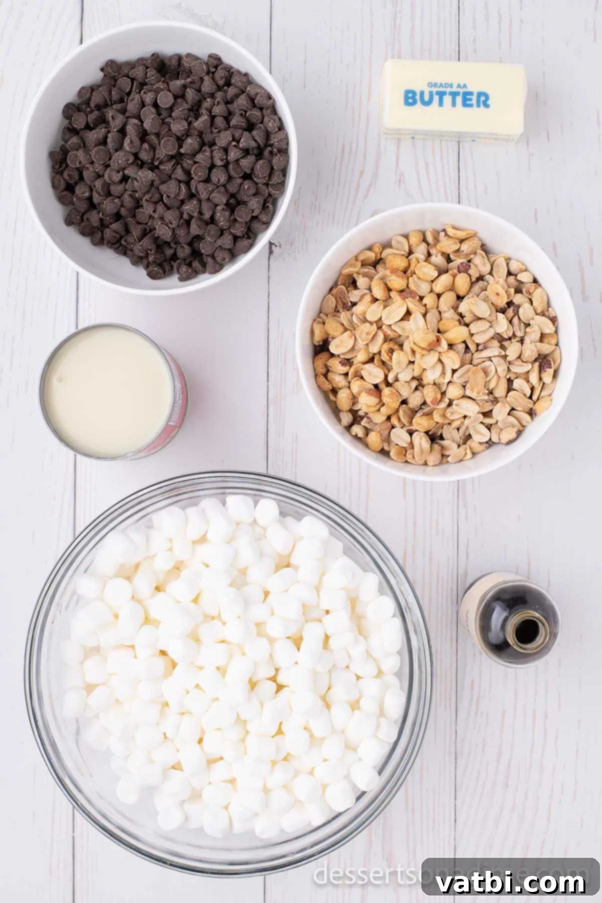Decadent Rocky Road 3 A flat lay photograph showcasing the five key ingredients for Rocky Road Candy: semi-sweet chocolate chips, butter, a can of sweetened condensed milk, dry roasted peanuts, and a bag of mini marshmallows.